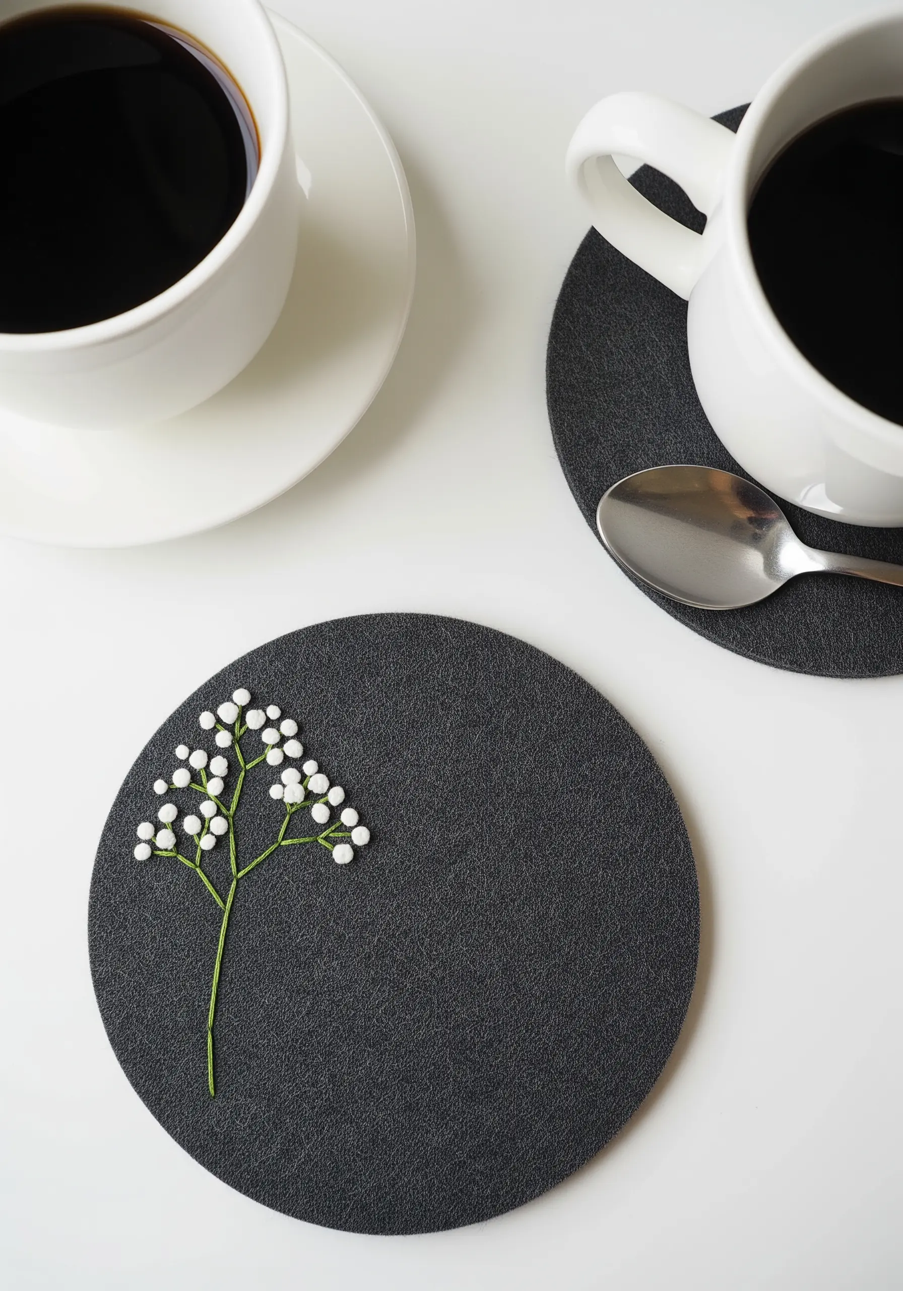 Minimalist baby's breath embroidery with white French knots on a black felt coaster.