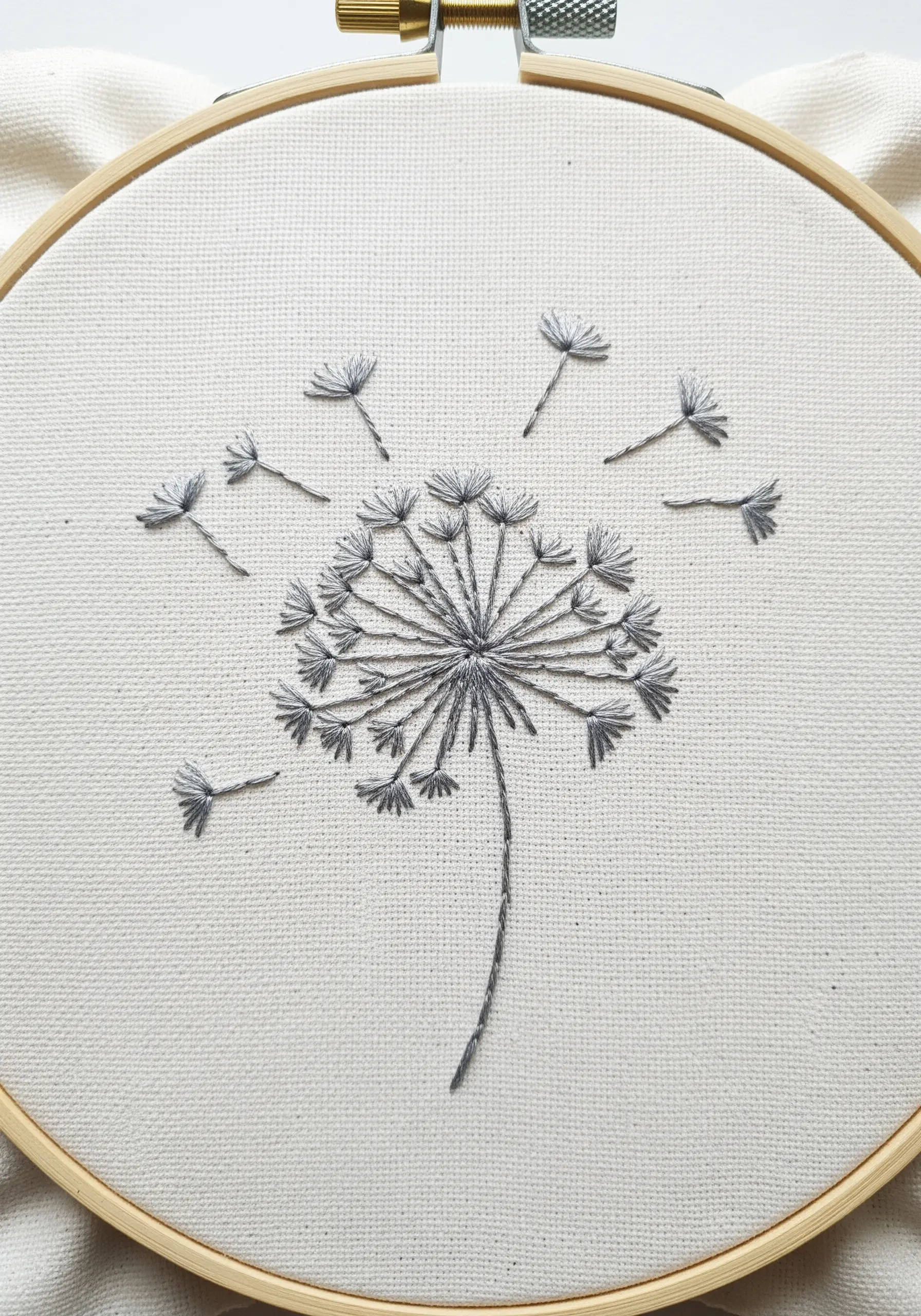 Line art dandelion with detached chain stitches for seeds on white canvas.