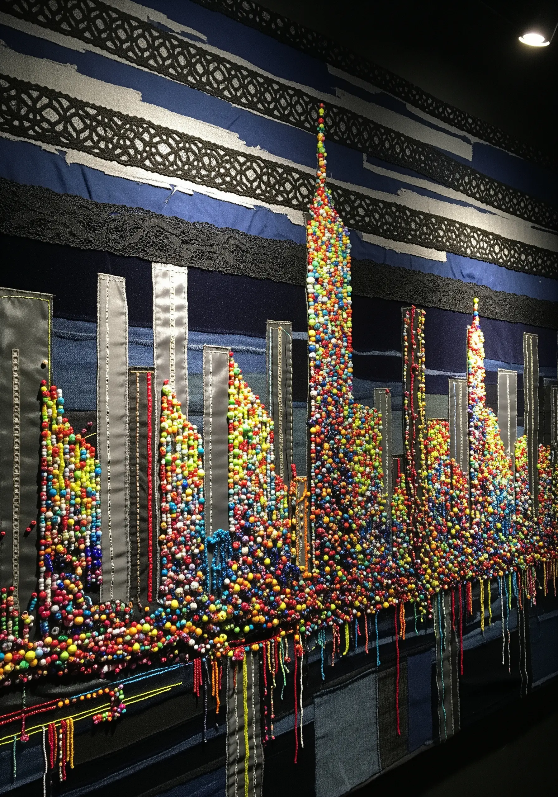 A textile cityscape with building silhouettes filled with a dense collage of colorful beads.