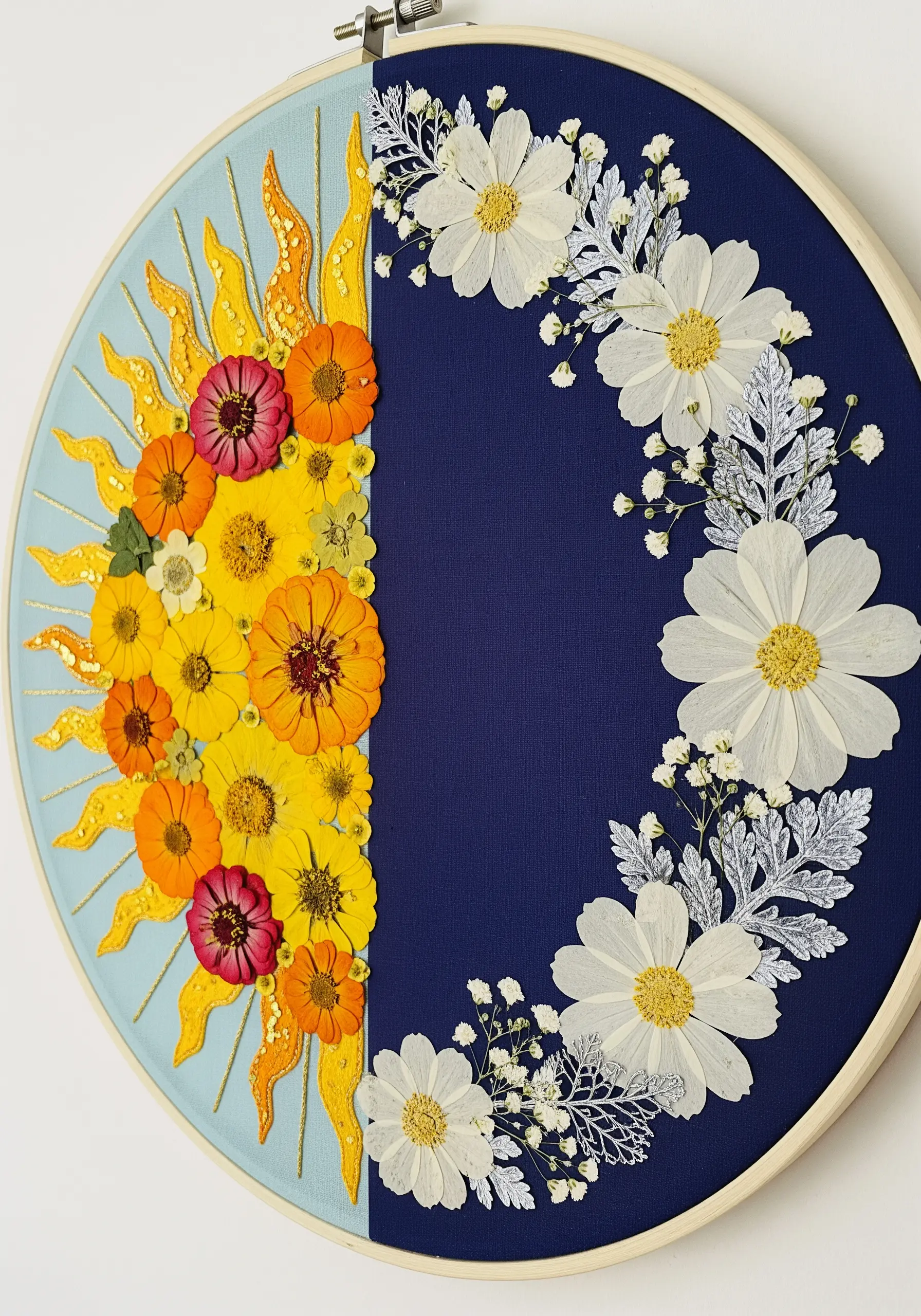 A hoop split into two halves: one with an embroidered sun and orange flowers, the other with white flowers.