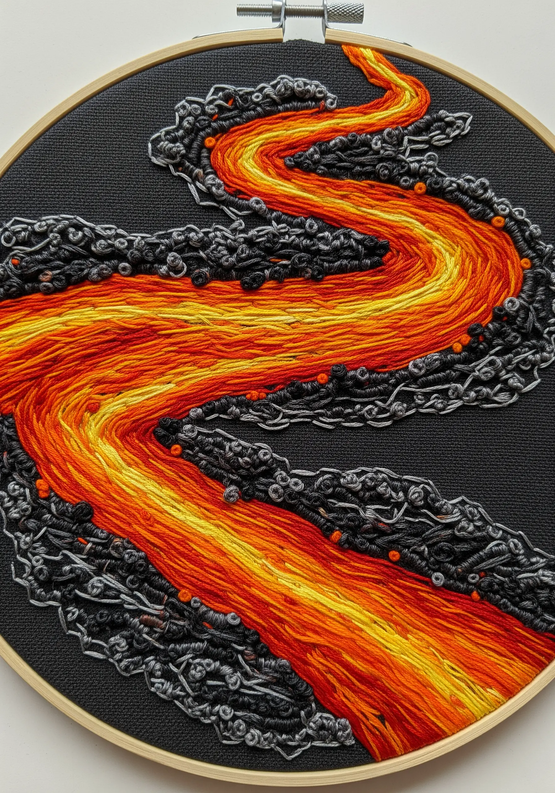 Embroidery of a lava river with fiery satin stitches and textured grey knots for rocks.