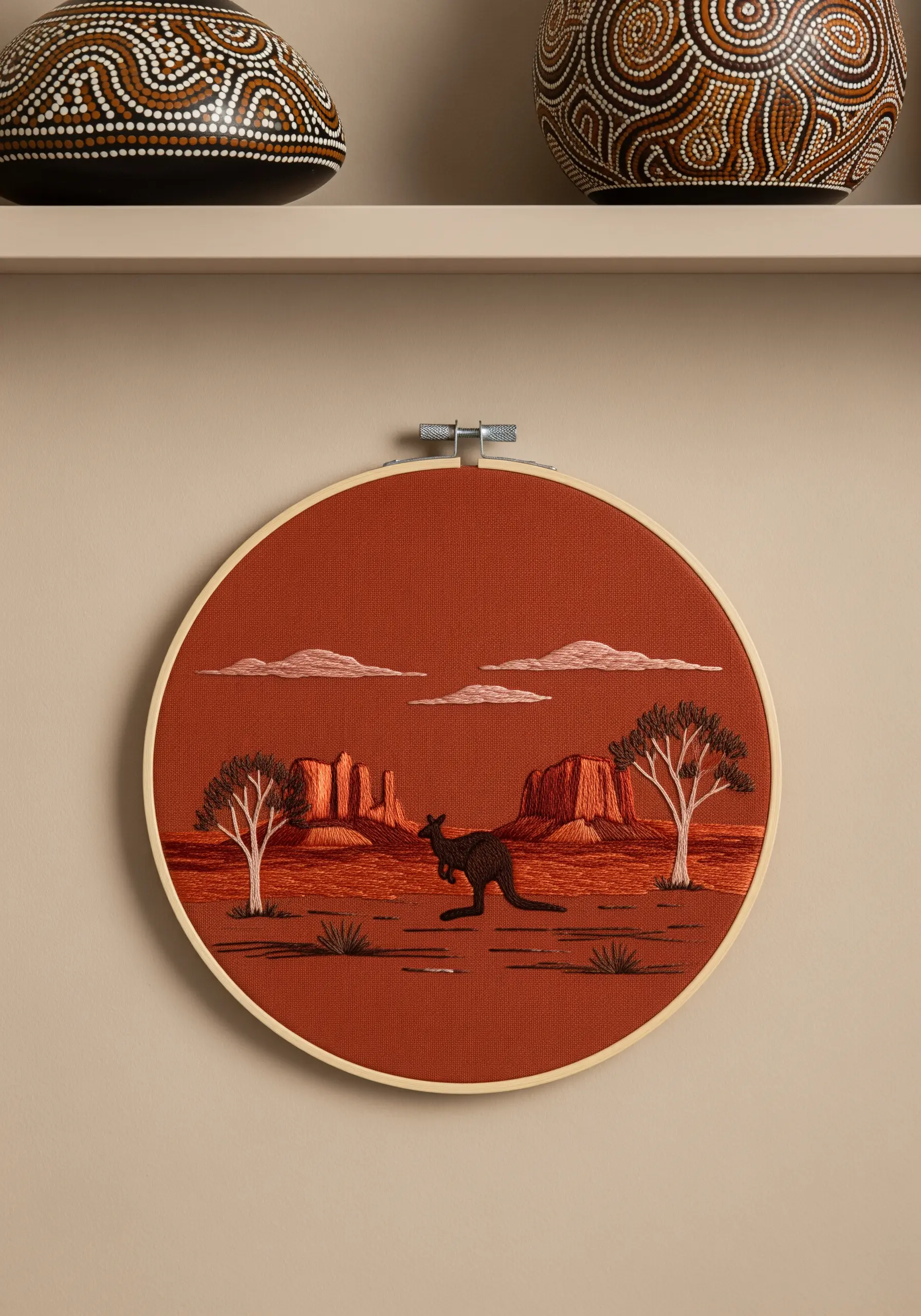 Monochromatic embroidery of the Australian outback with a kangaroo on rust-colored fabric.