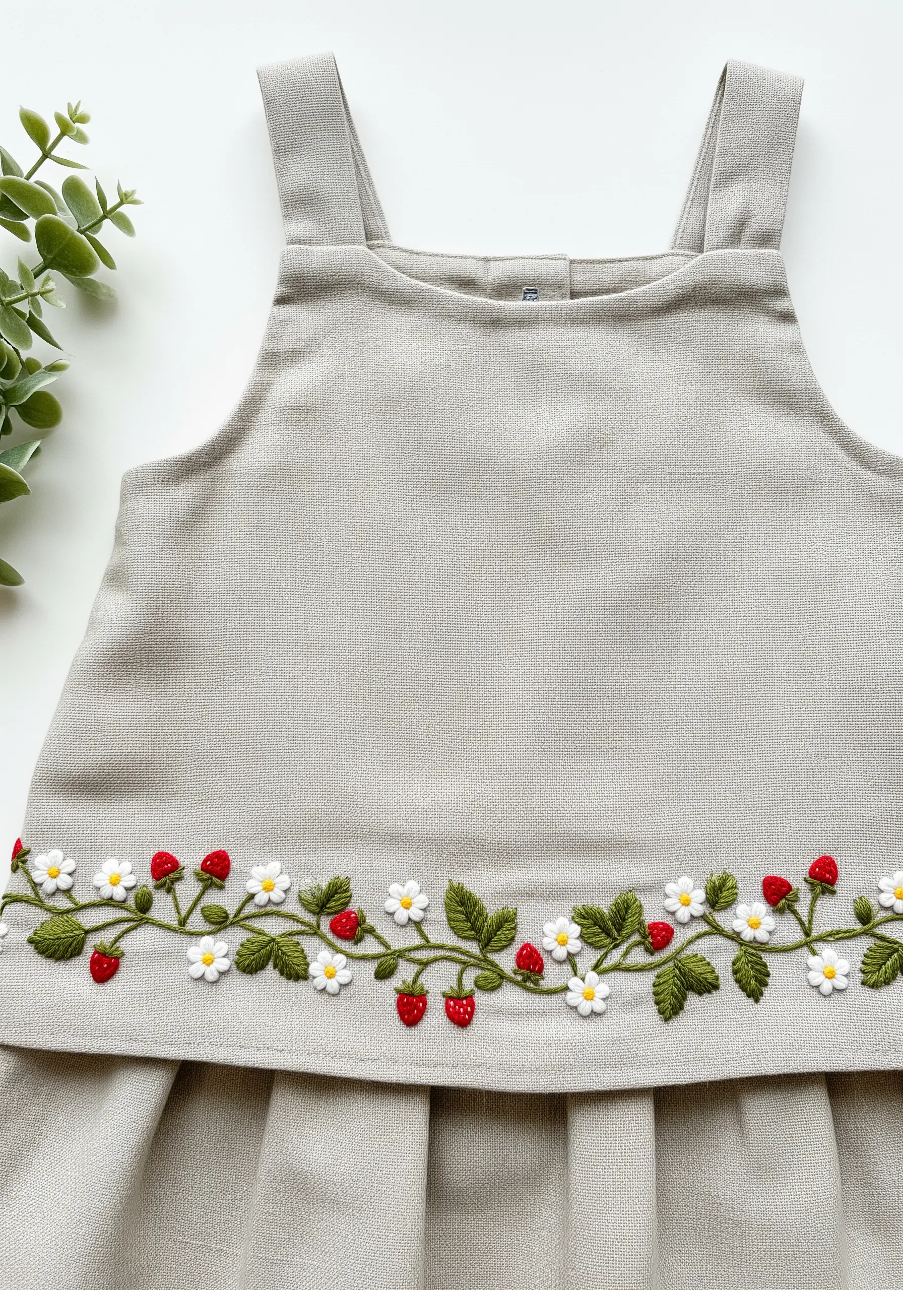 A border of embroidered strawberries, white flowers, and green leaves on a linen dress.