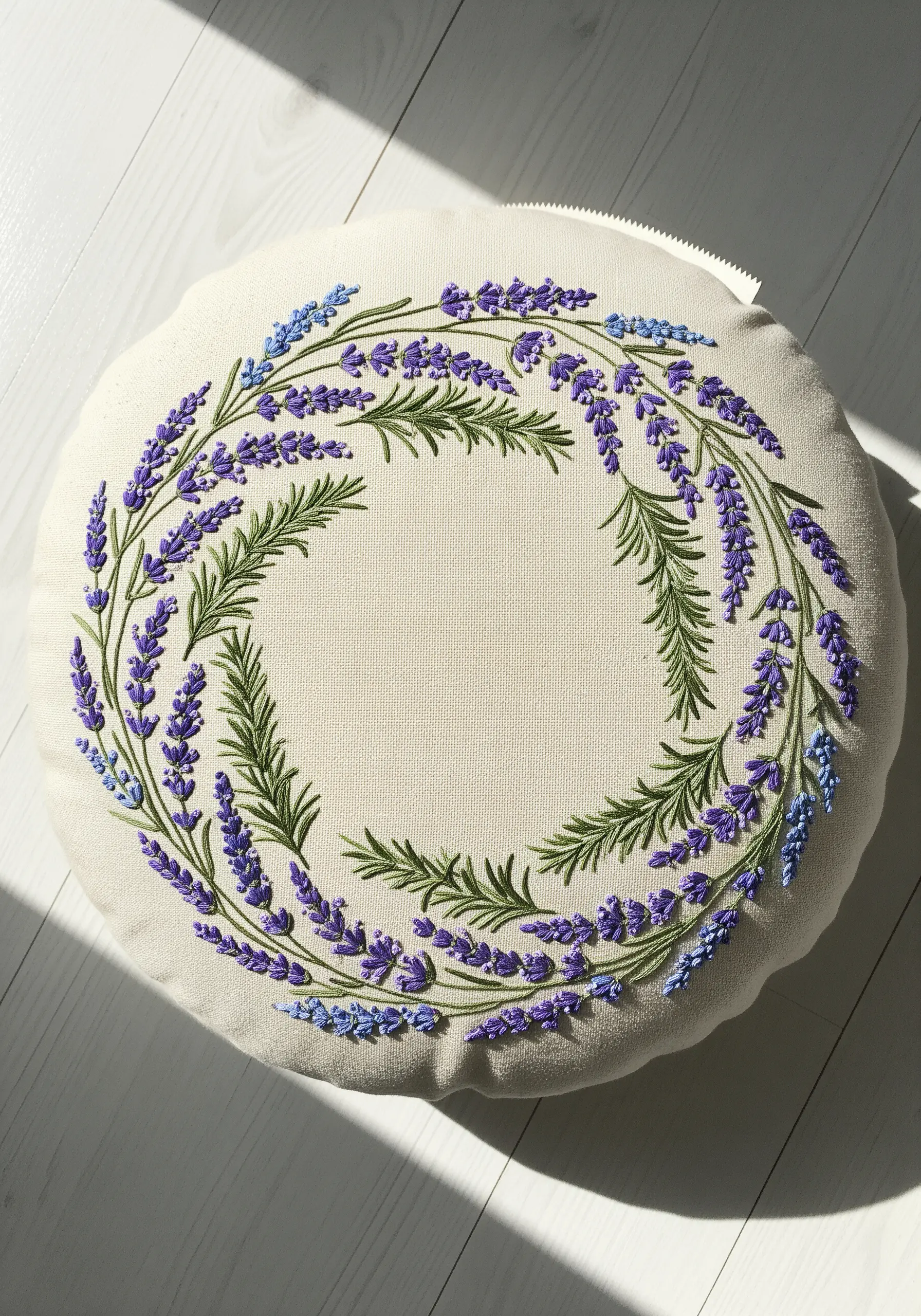 A delicate wreath of embroidered lavender and rosemary on a round white pillow.