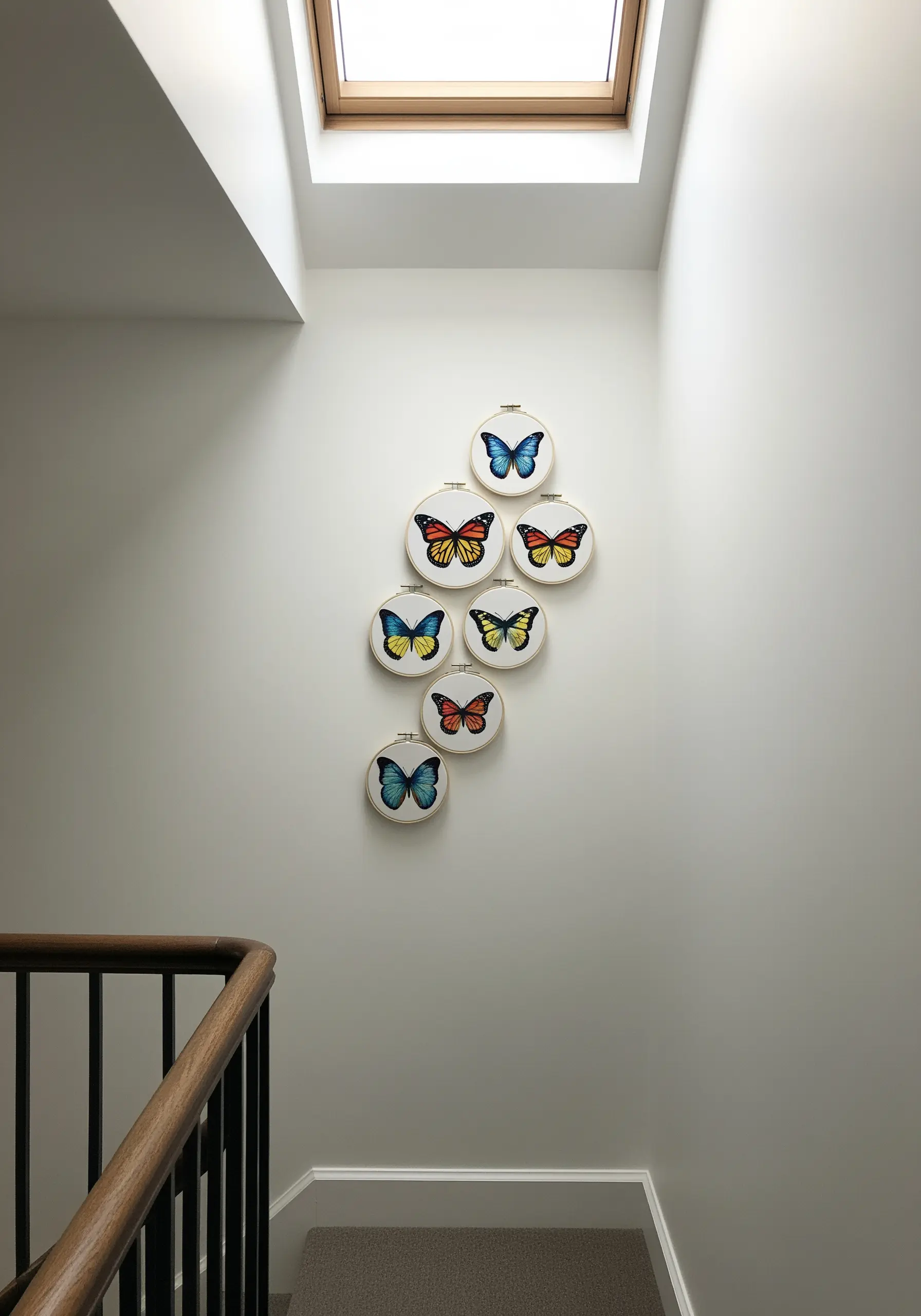 A cluster of six embroidery hoops with colorful butterflies arranged in a cascading pattern on a stairwell.