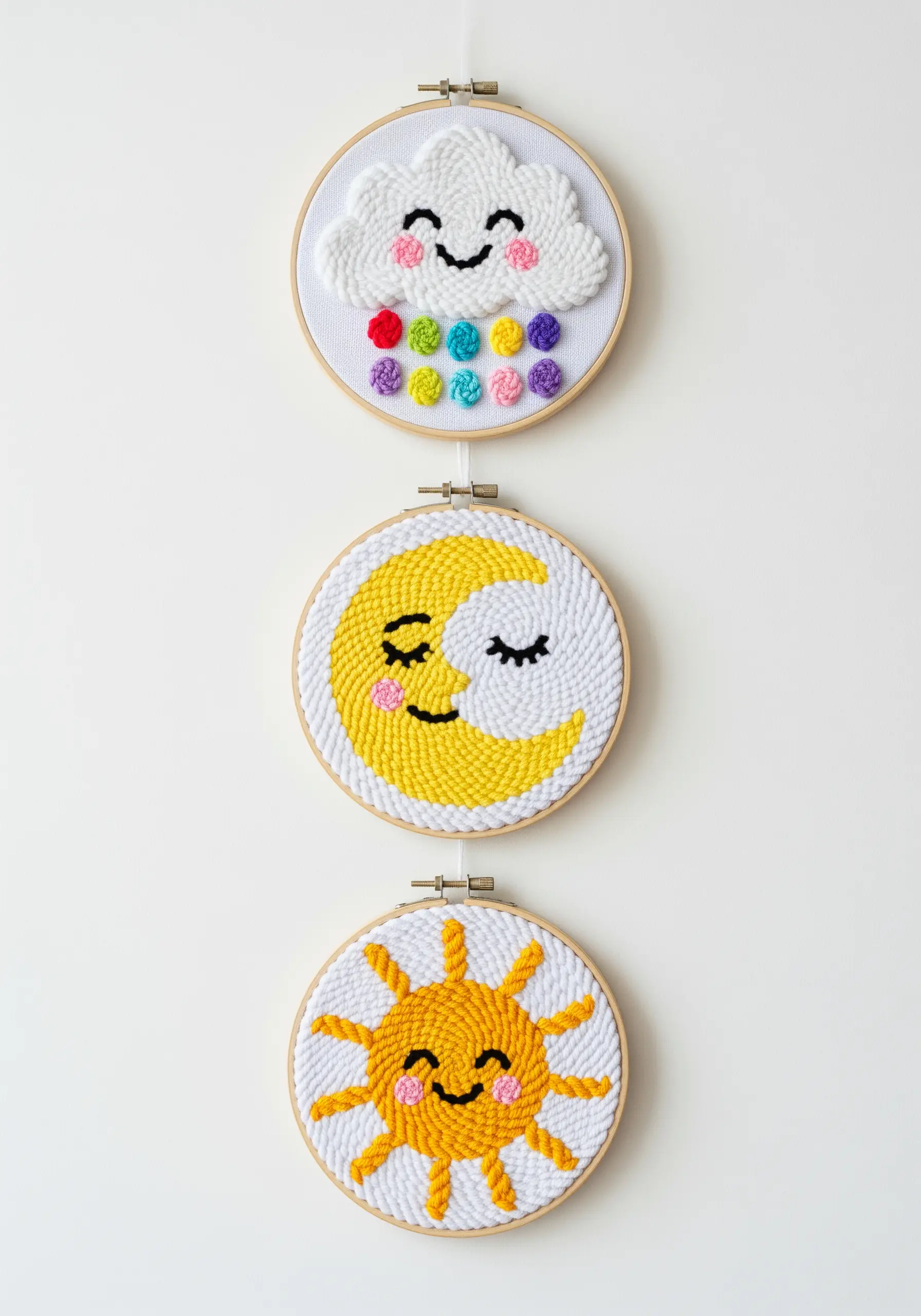 A set of three punch needle embroidery hoops showing a cloud, moon, and sun.