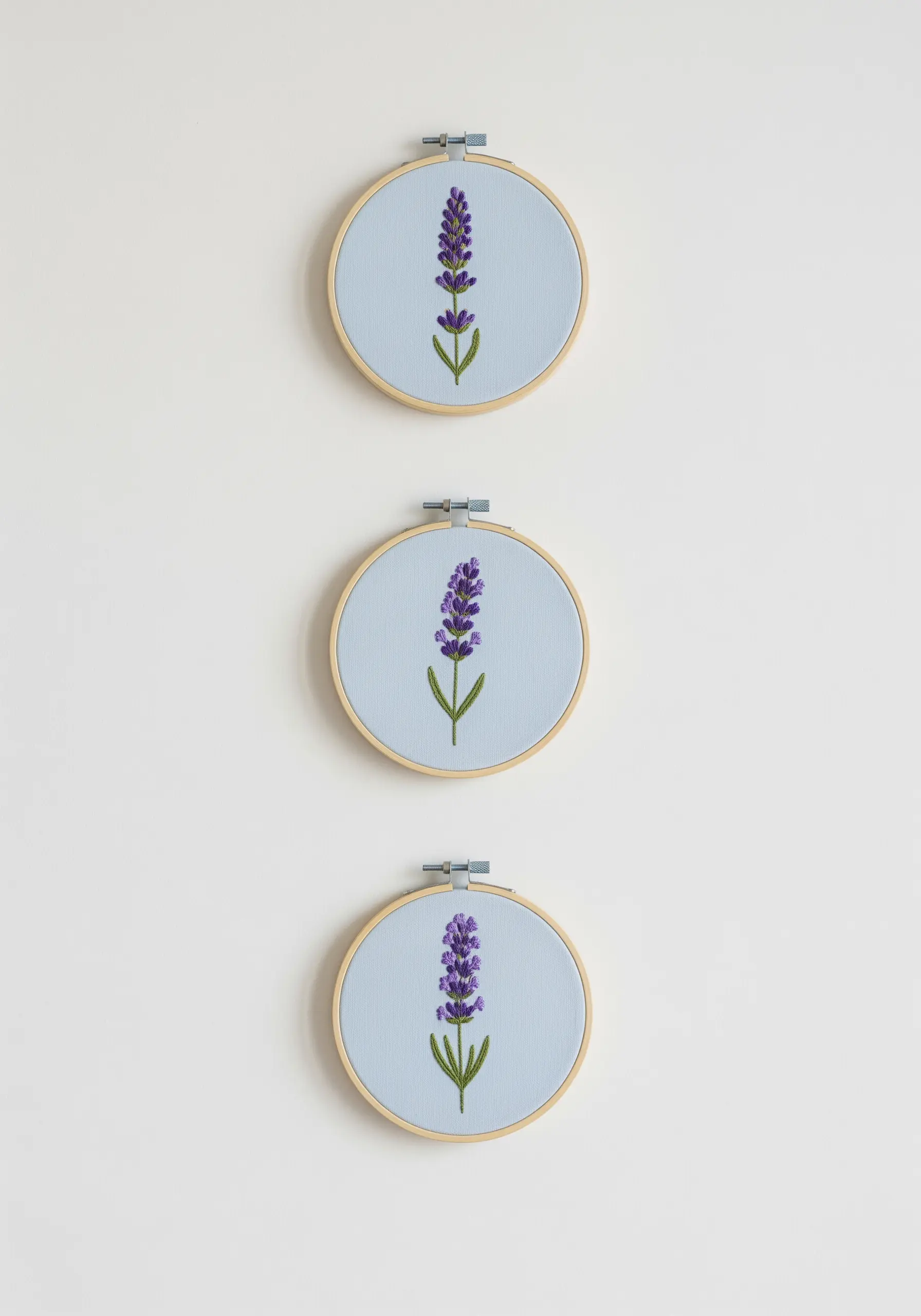 A vertical series of three small embroidery hoops, each with a single lavender sprig.