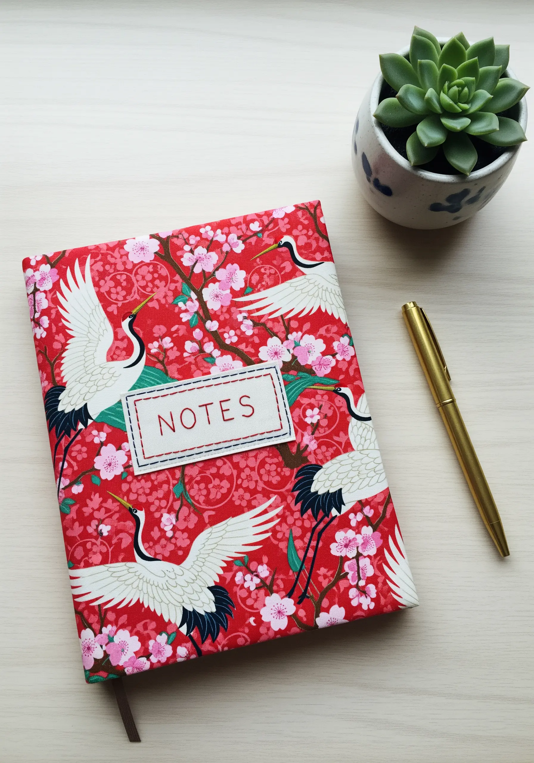 A journal covered in red fabric with a crane and cherry blossom pattern.