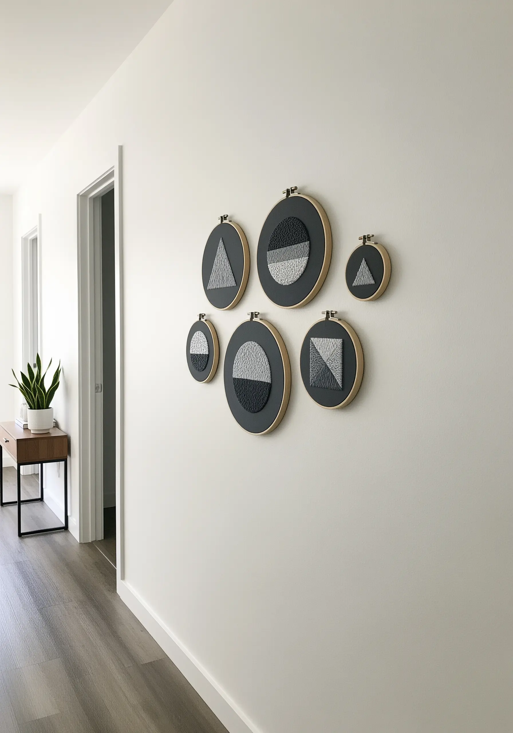 A gallery wall of six small embroidery hoops with geometric designs in charcoal and grey.