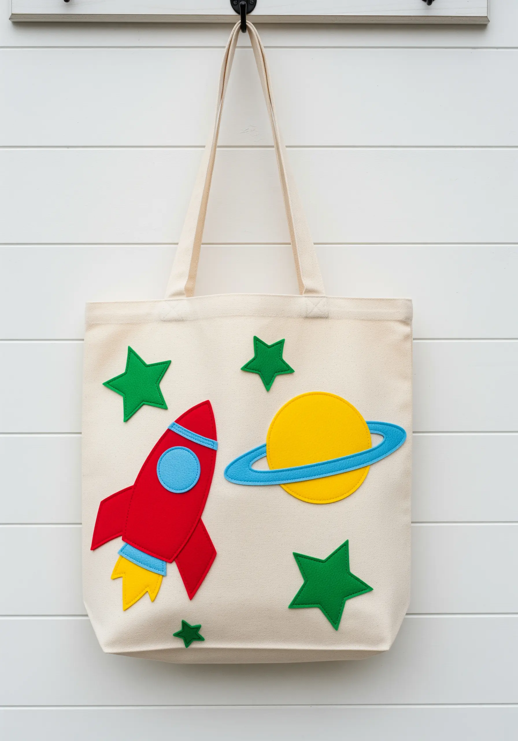 A canvas tote bag decorated with a felt rocket, planet, and stars.