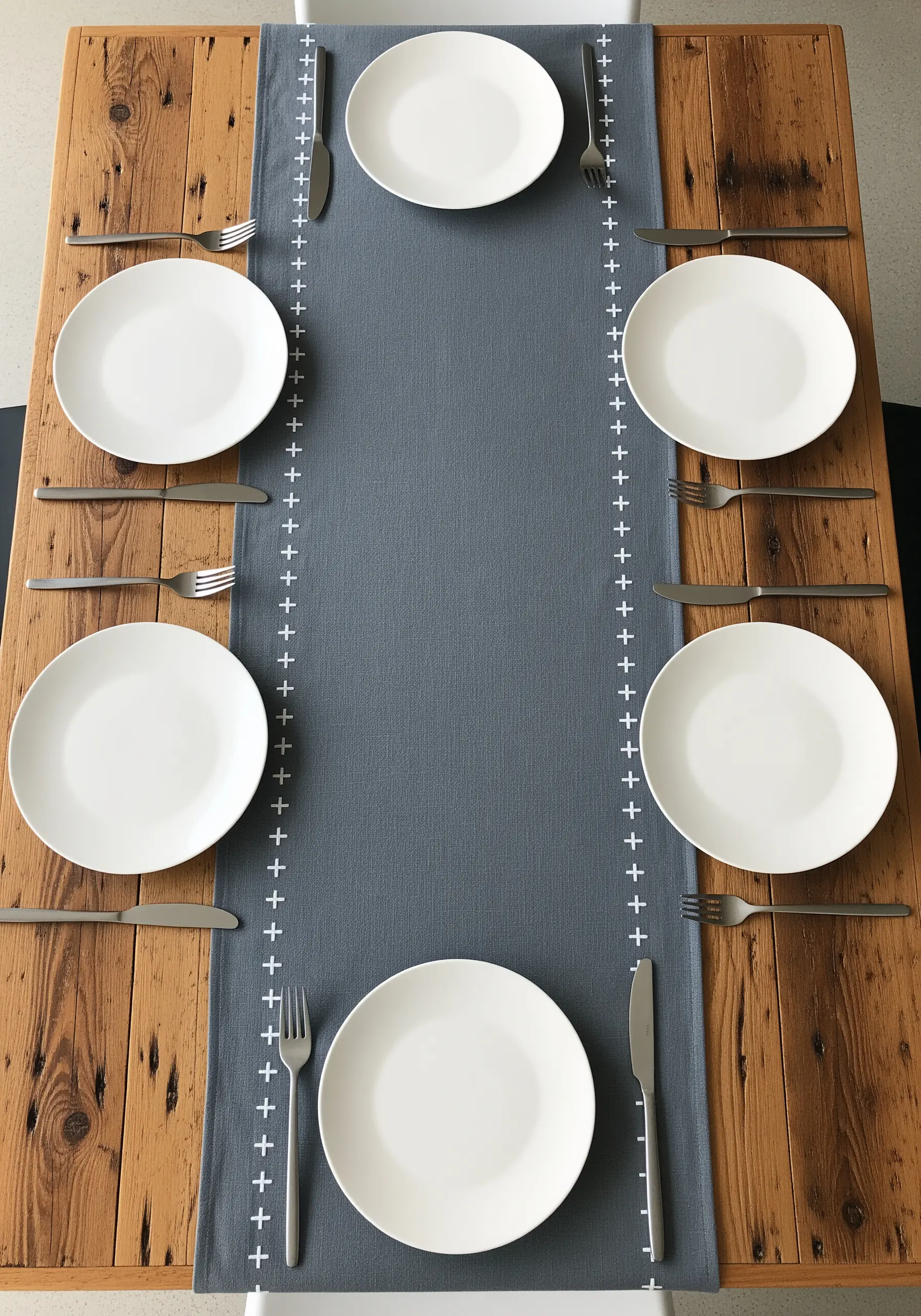 Grey linen table runner with a minimalist white embroidered border of plus signs and lines.