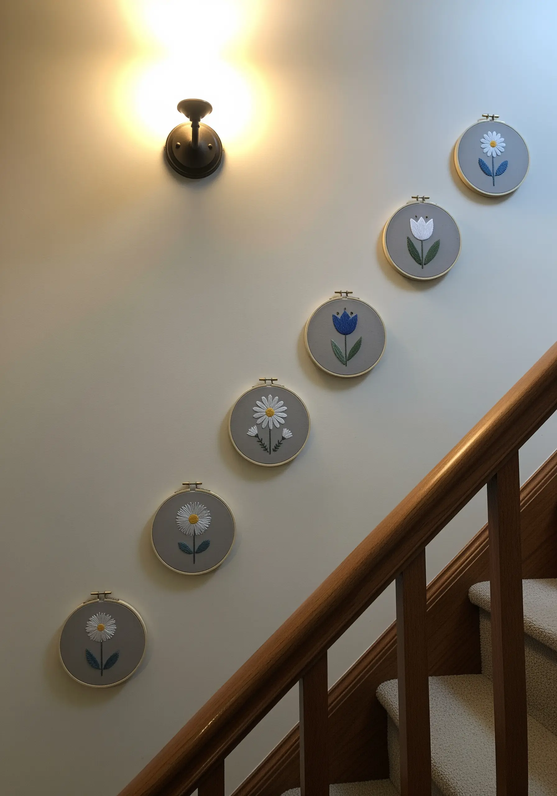 A series of minimalist floral embroidery hoops arranged along a staircase wall.