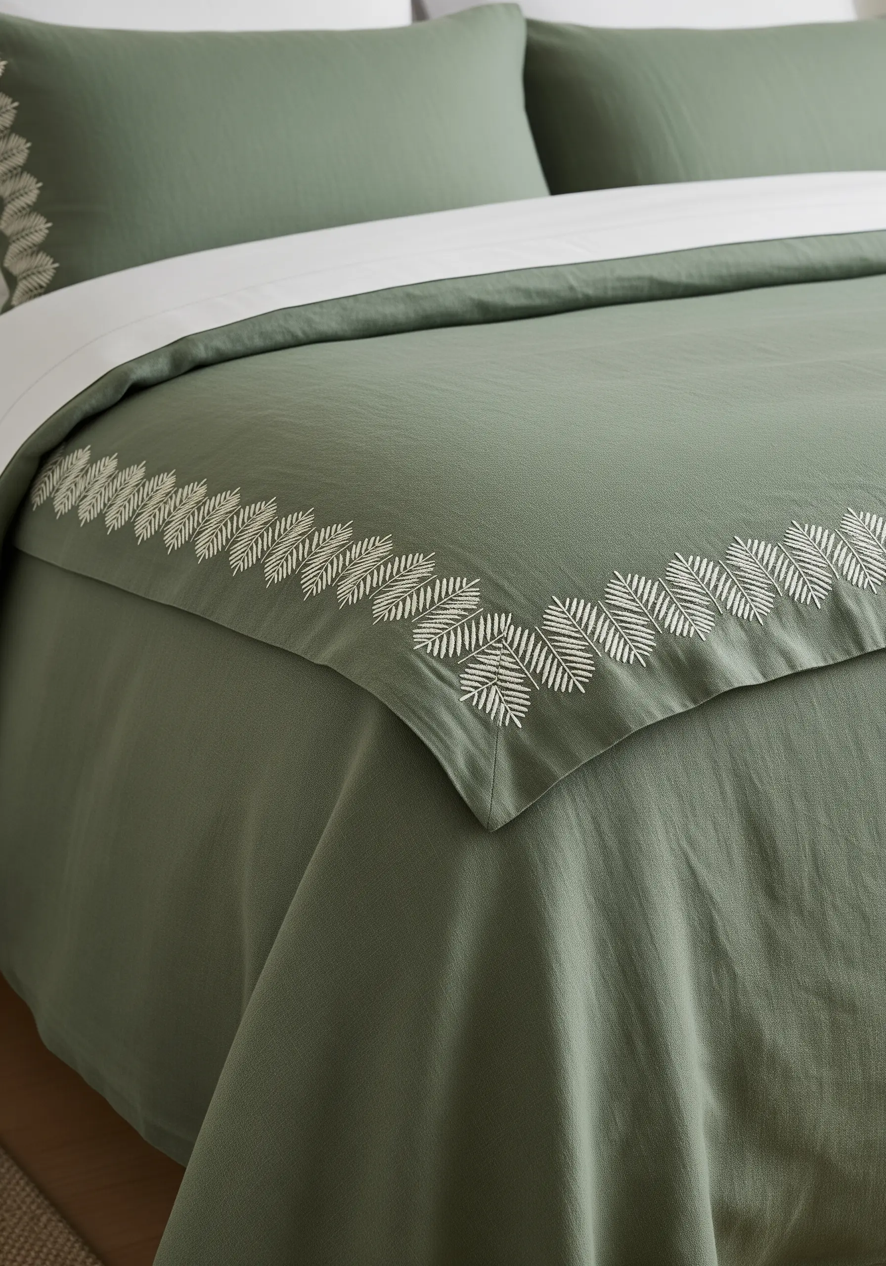 A border of stylized white leaves on a sage green duvet cover, made with fishbone stitch.