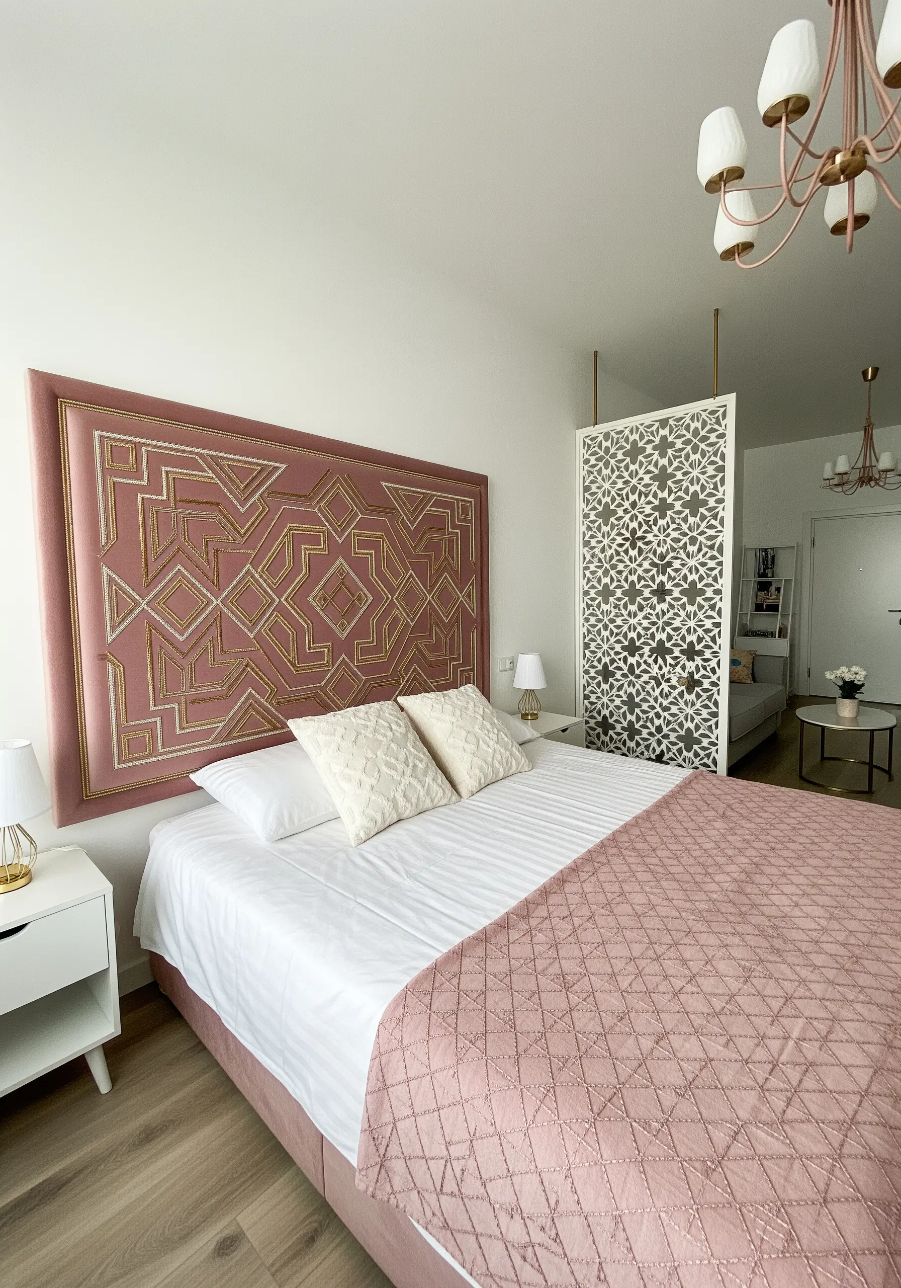 A dusty rose upholstered headboard with an intricate geometric pattern embroidered in gold thread.