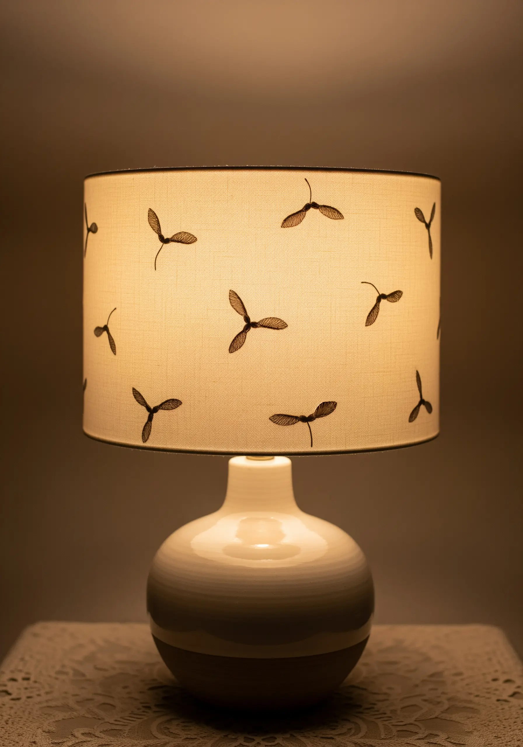 Small, dark seed pod motifs embroidered randomly on a cream-colored lampshade.
