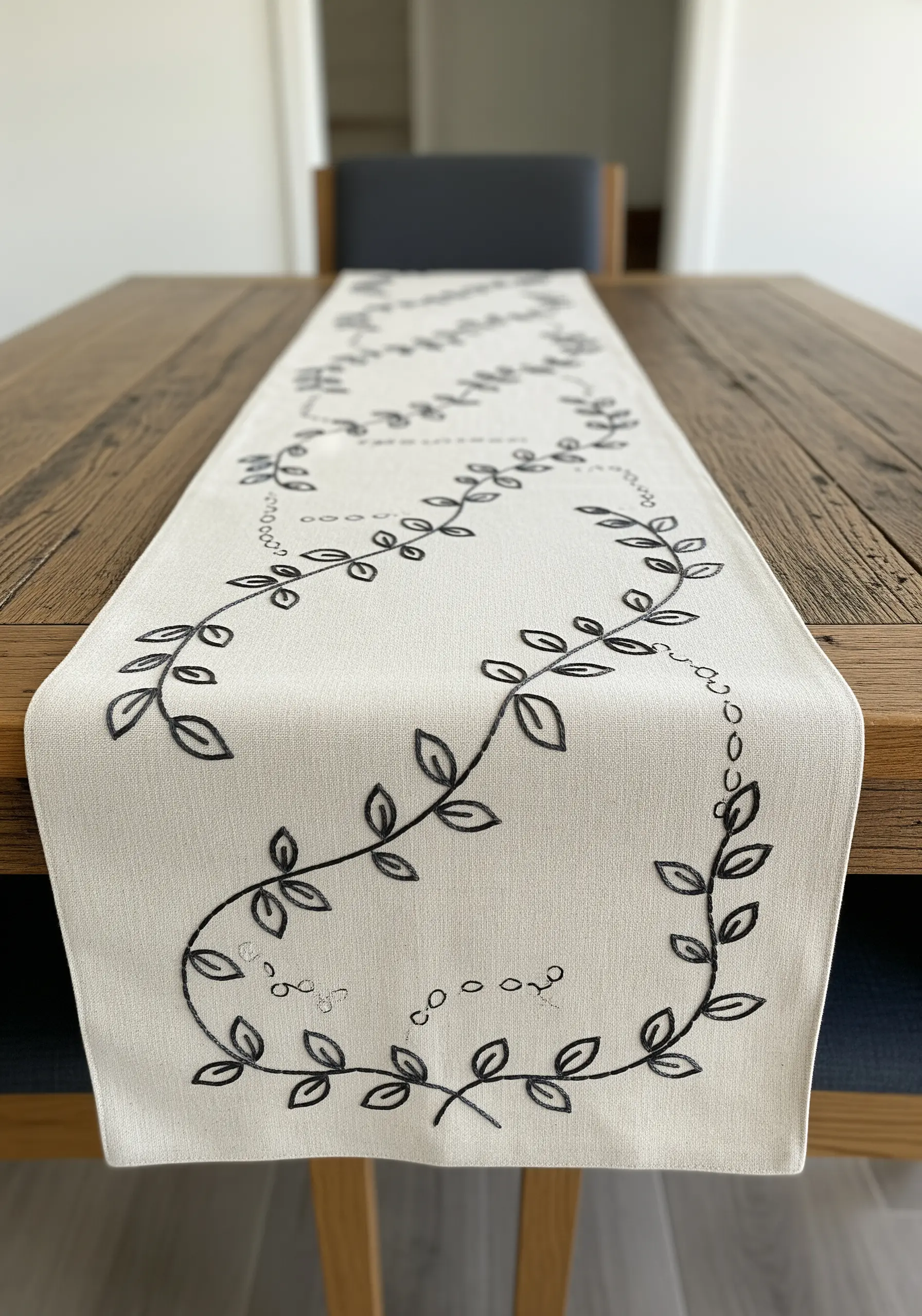 A long table runner with a simple, meandering vine embroidered in black thread.