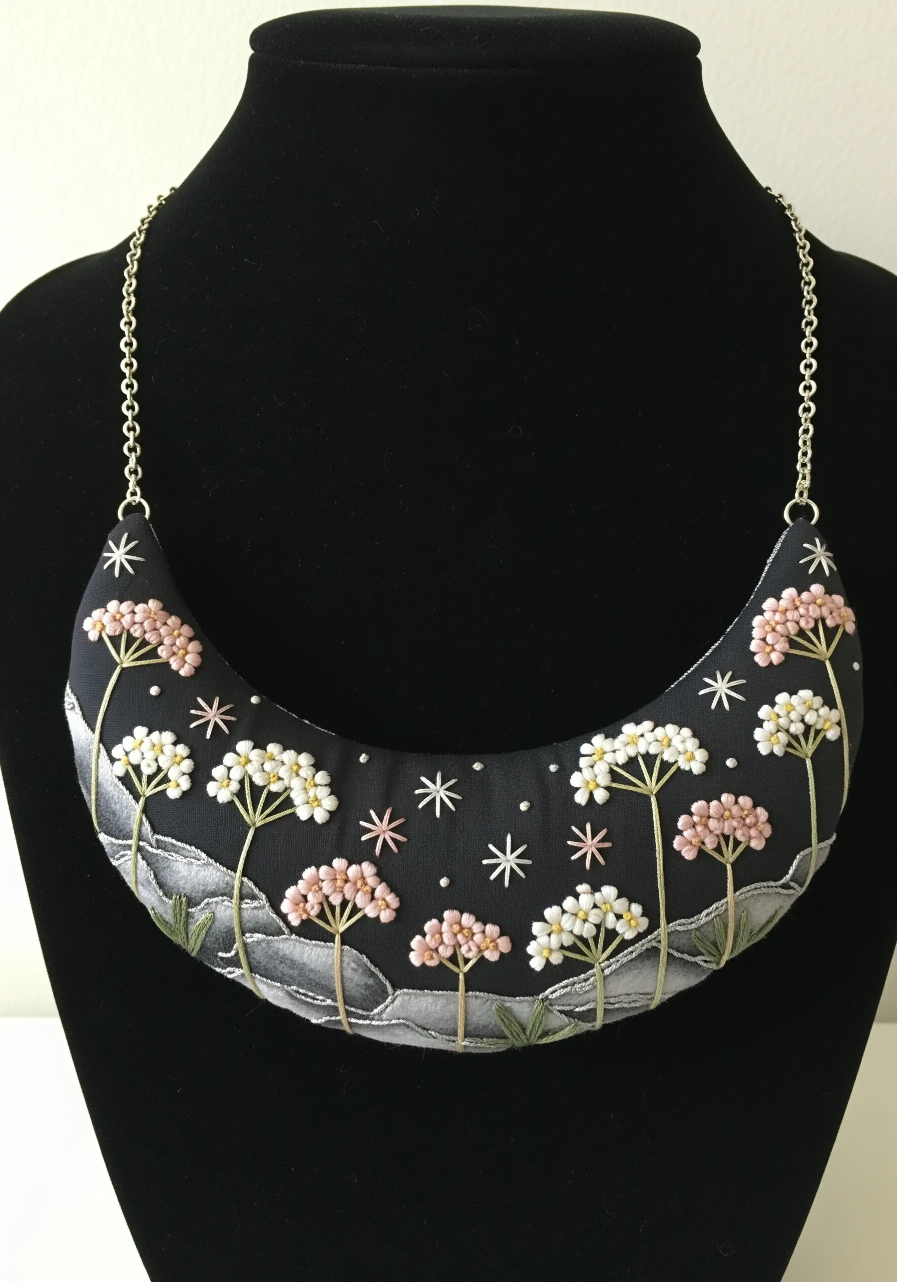 A crescent-shaped necklace with embroidered Queen Anne's Lace flowers on a black background