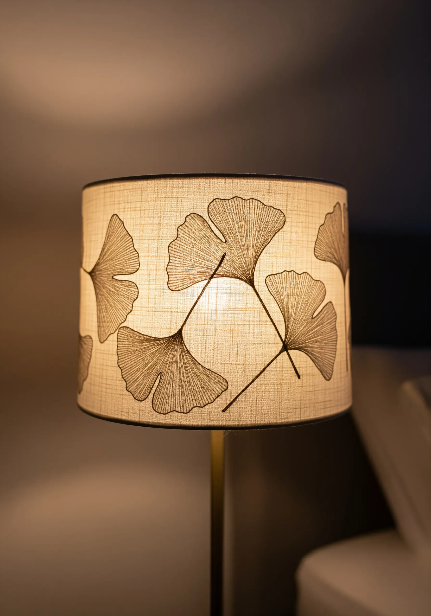 A lit drum lampshade with an embroidered pattern of minimalist ginkgo leaves.