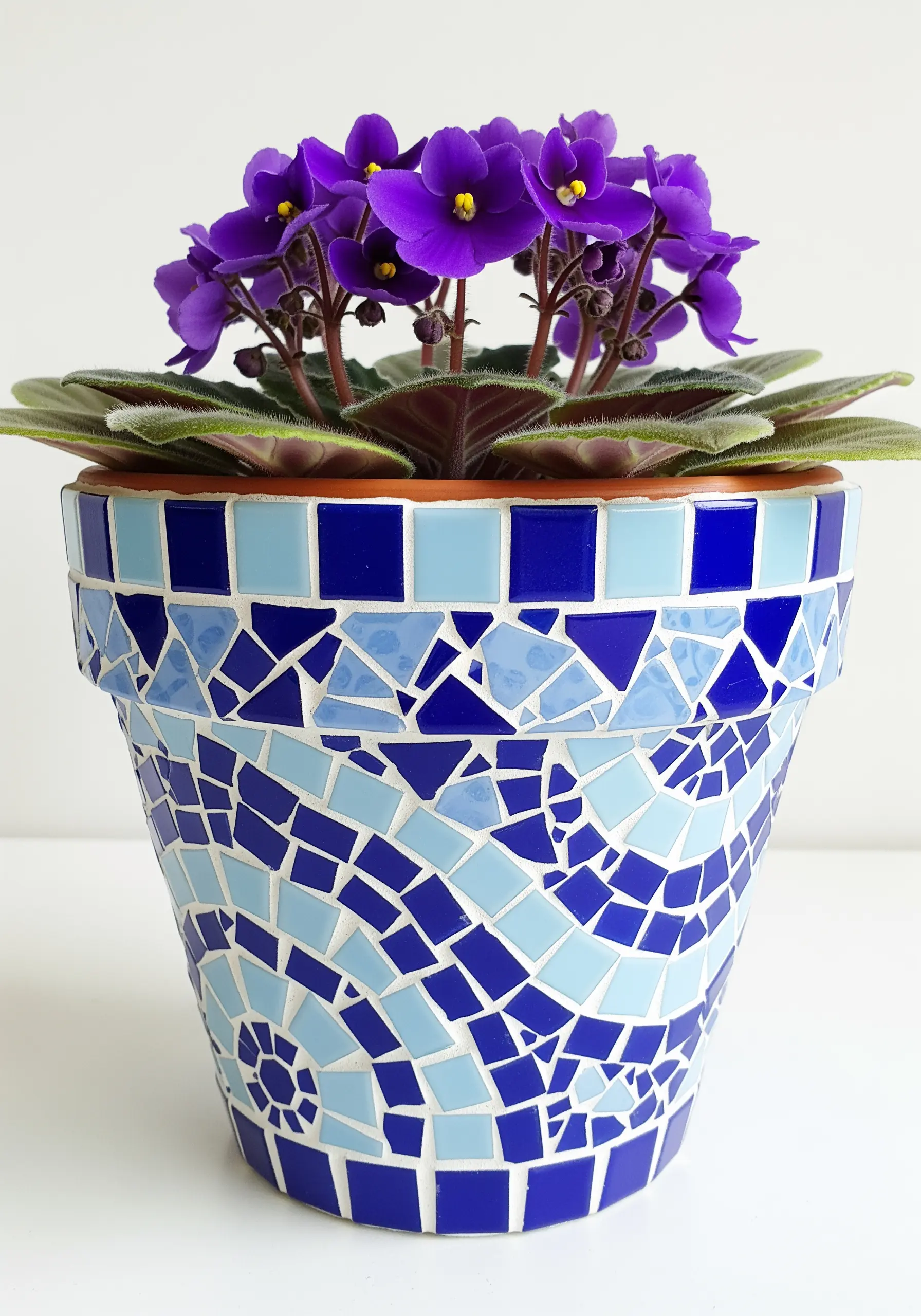 A flowerpot decorated with a mosaic of broken tiles in shades of blue, creating a gradient effect.