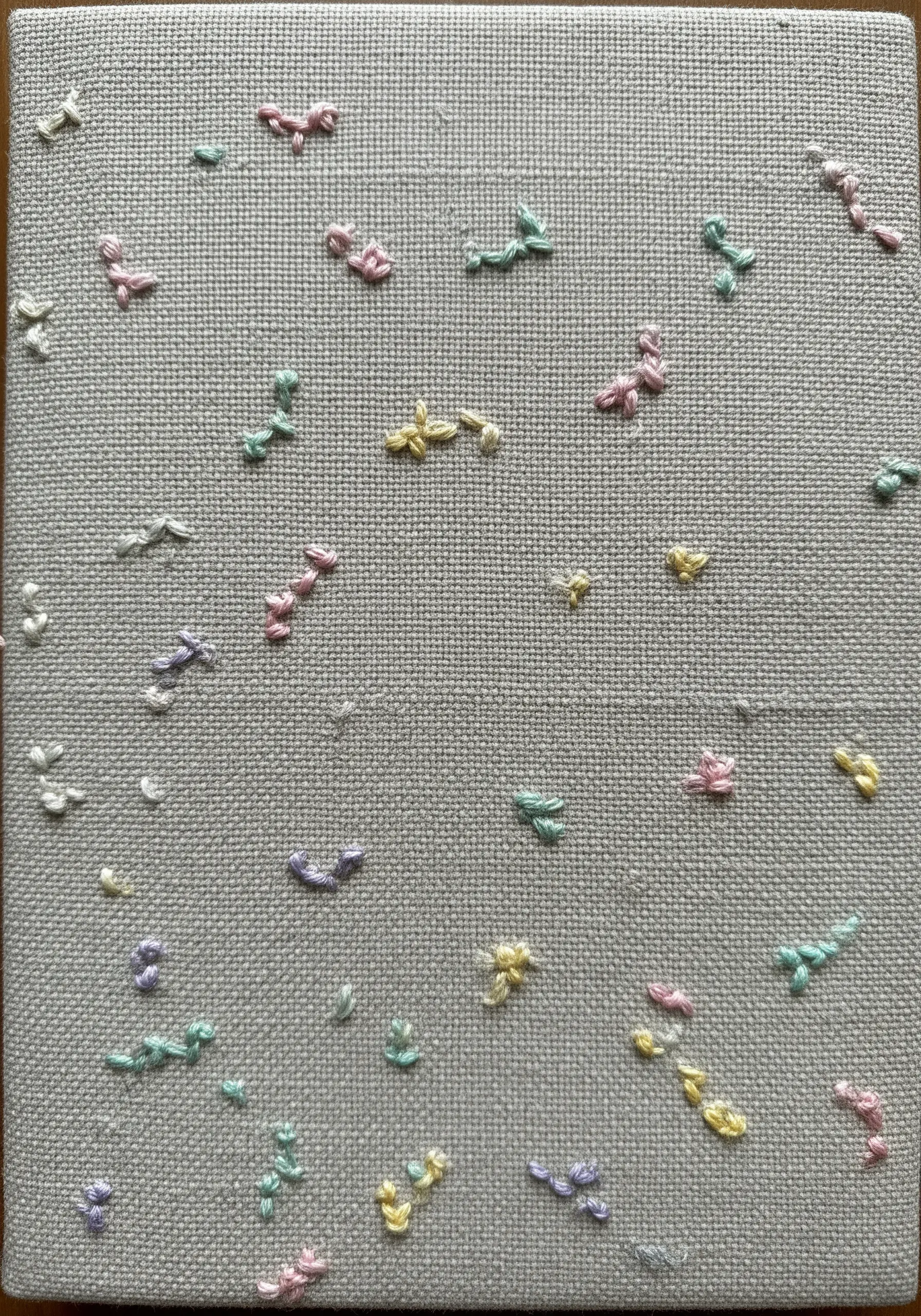 A random scattering of small, colorful stitches on a grey fabric notebook.