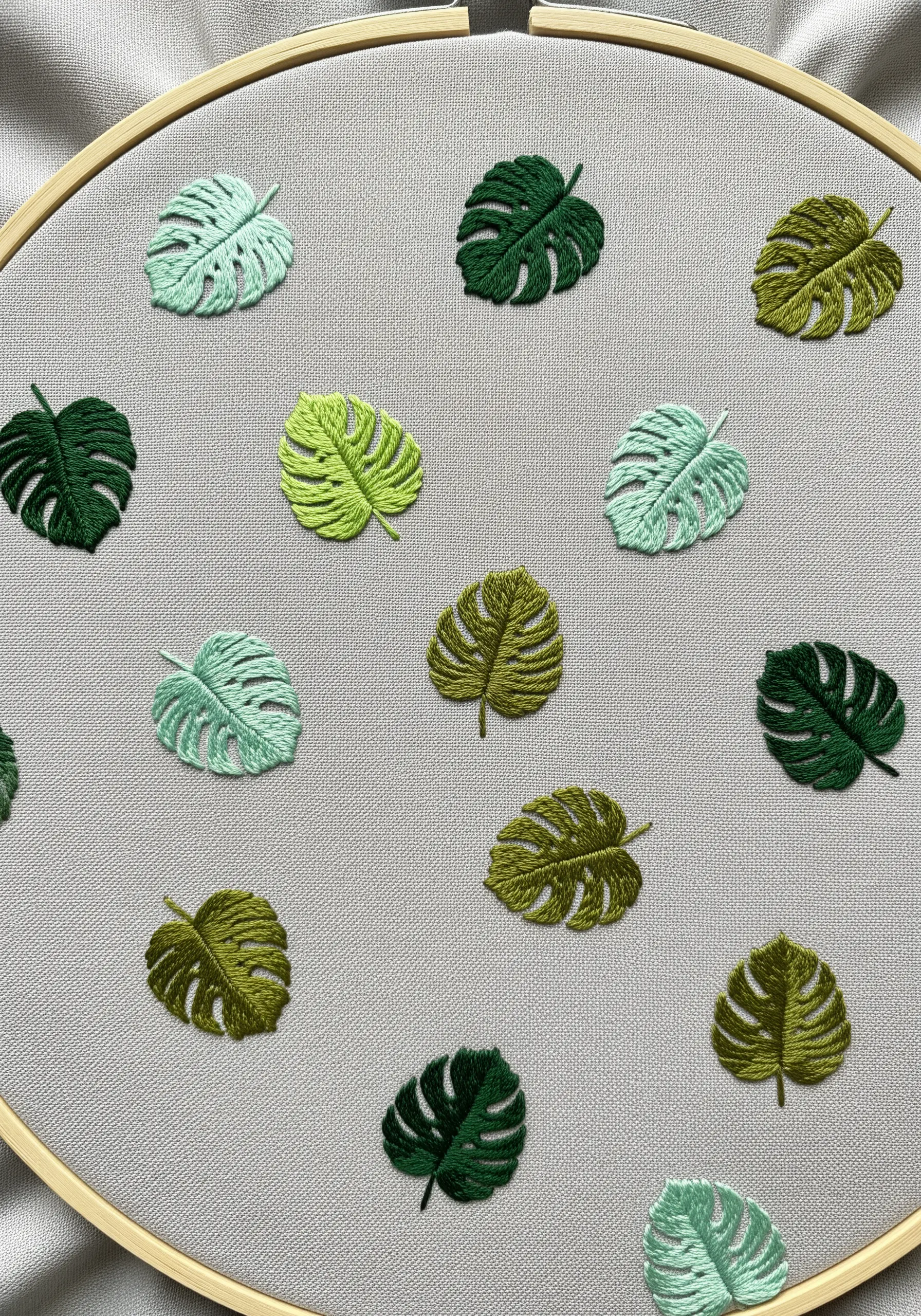 A scattered pattern of tiny embroidered Monstera leaves in various shades of green on gray fabric.