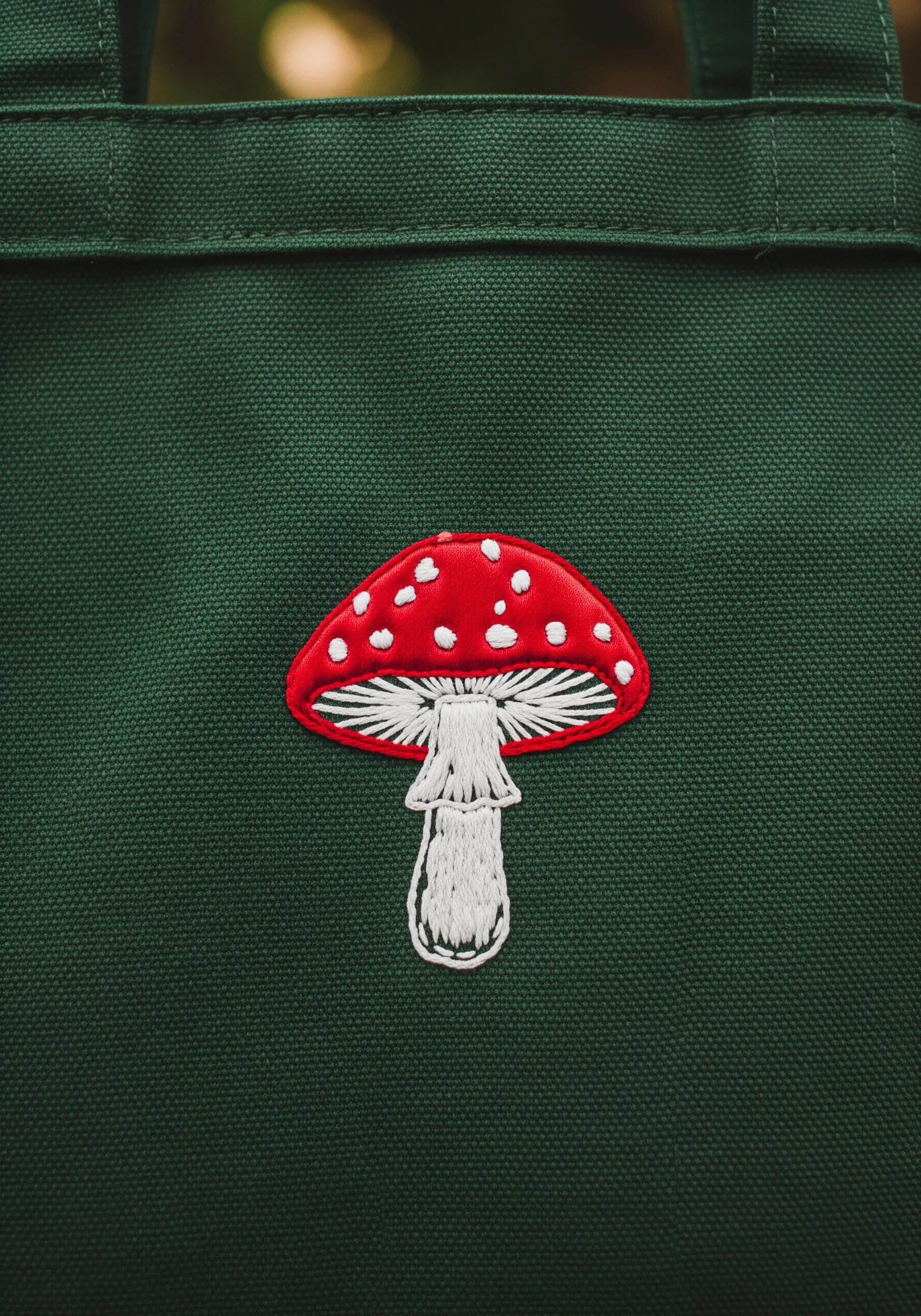 Embroidered red toadstool mushroom with white gills and spots on a dark green bag.