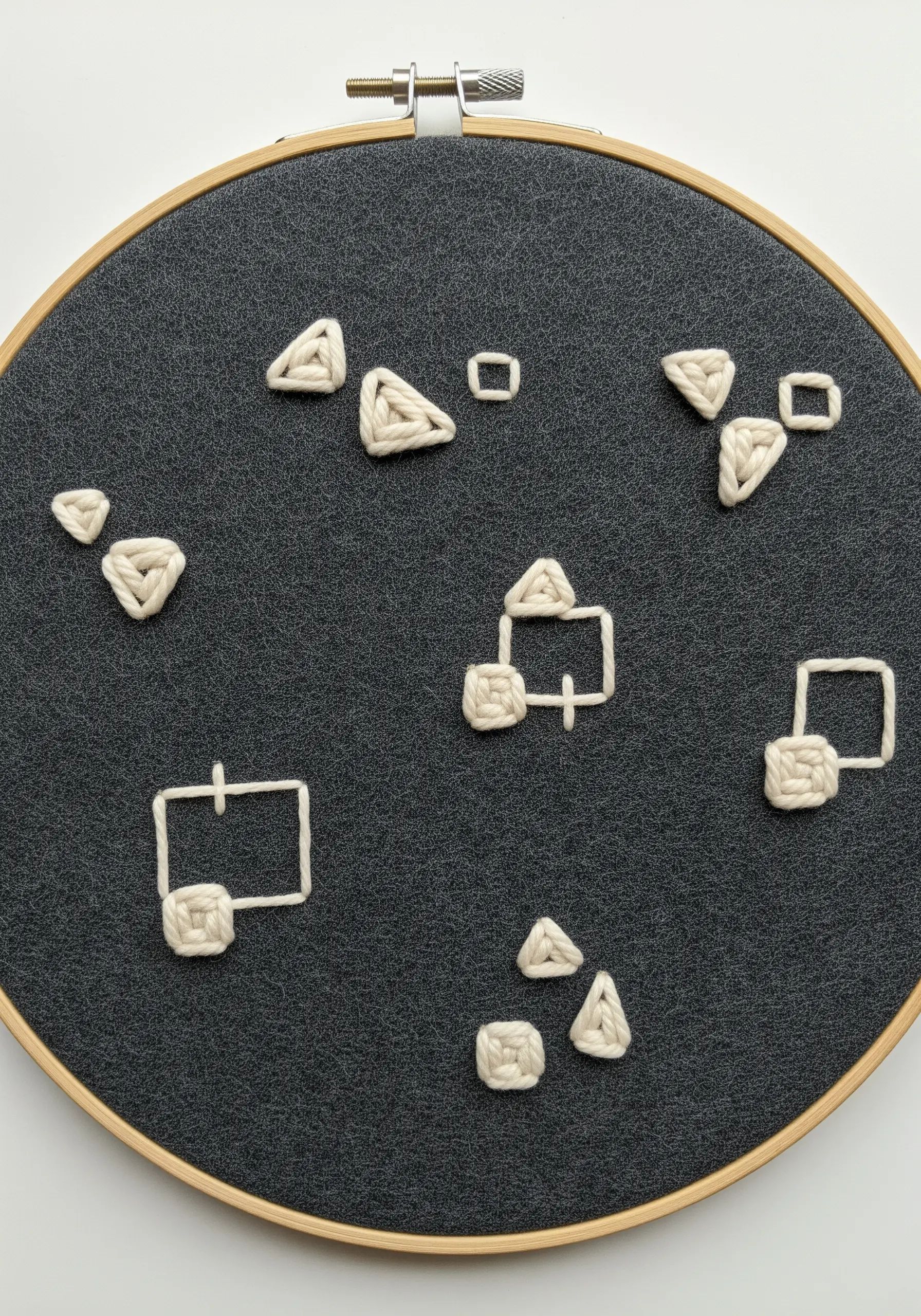 Chunky white yarn embroidery creating 3D geometric shapes on dark grey felt fabric.