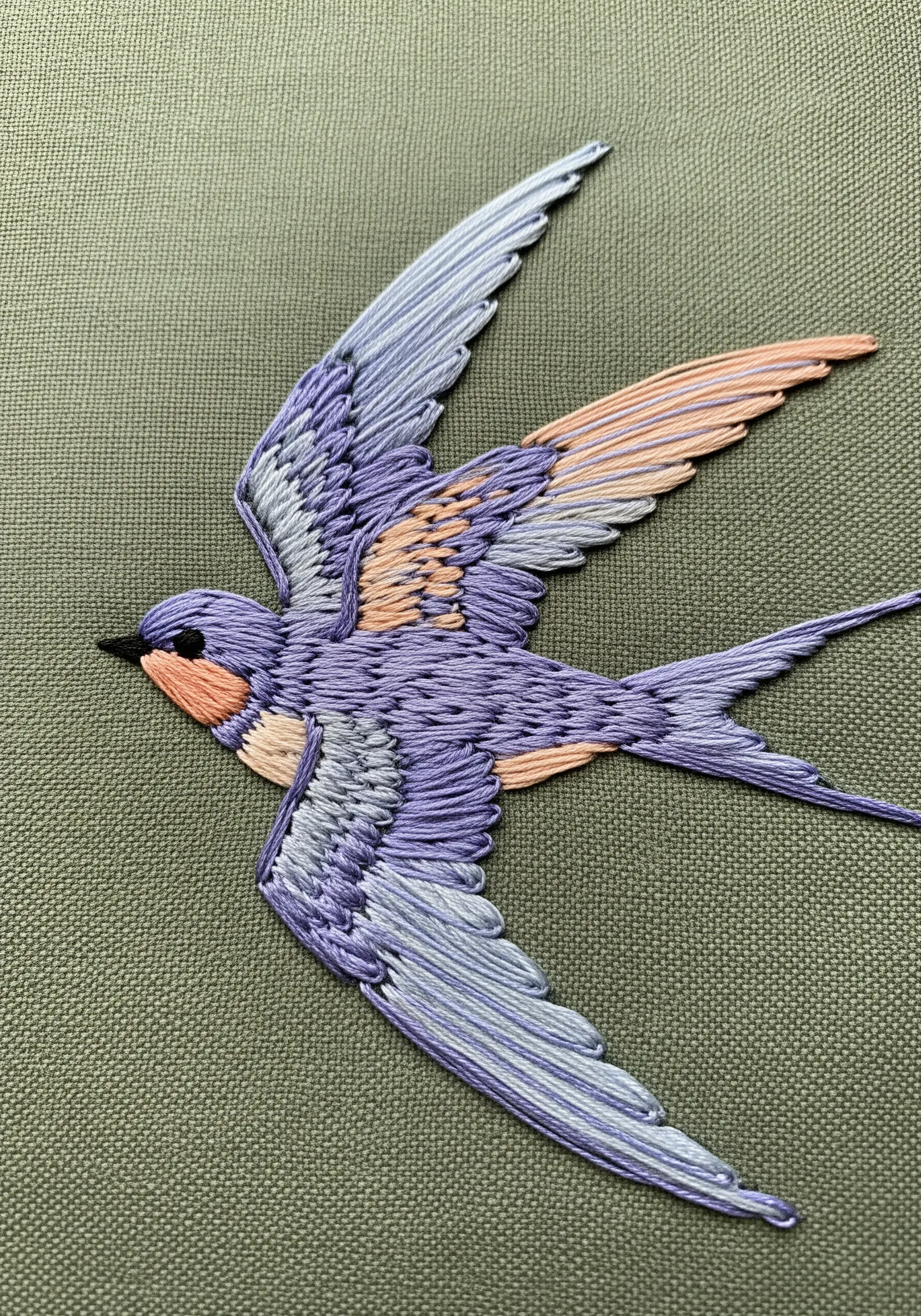 A swallow in flight, stitched with pastel threads that follow the direction of its feathers.