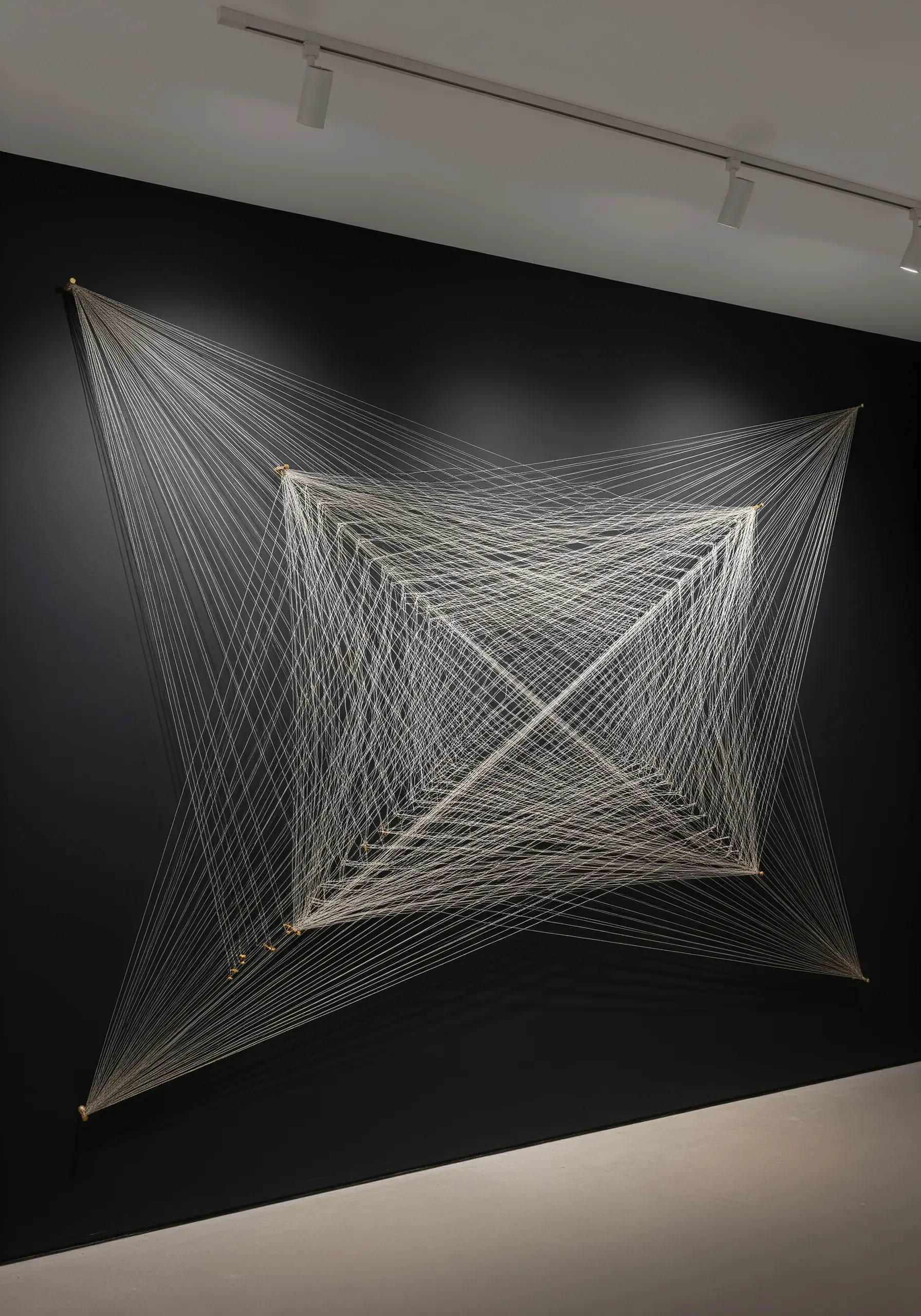A large-scale string art installation with white thread stretched between points on a black wall.