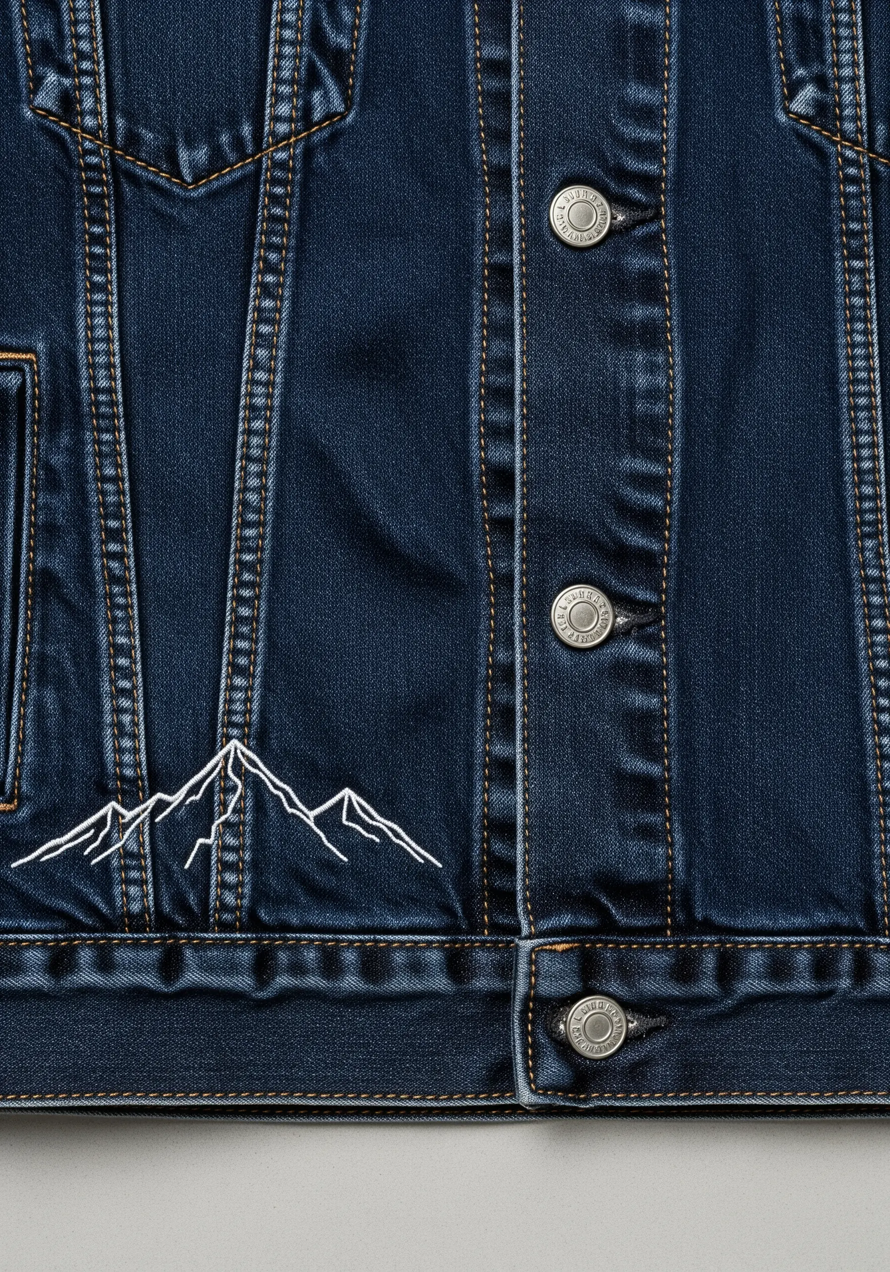 A minimalist white line-art embroidery of a mountain range on a dark denim jacket.