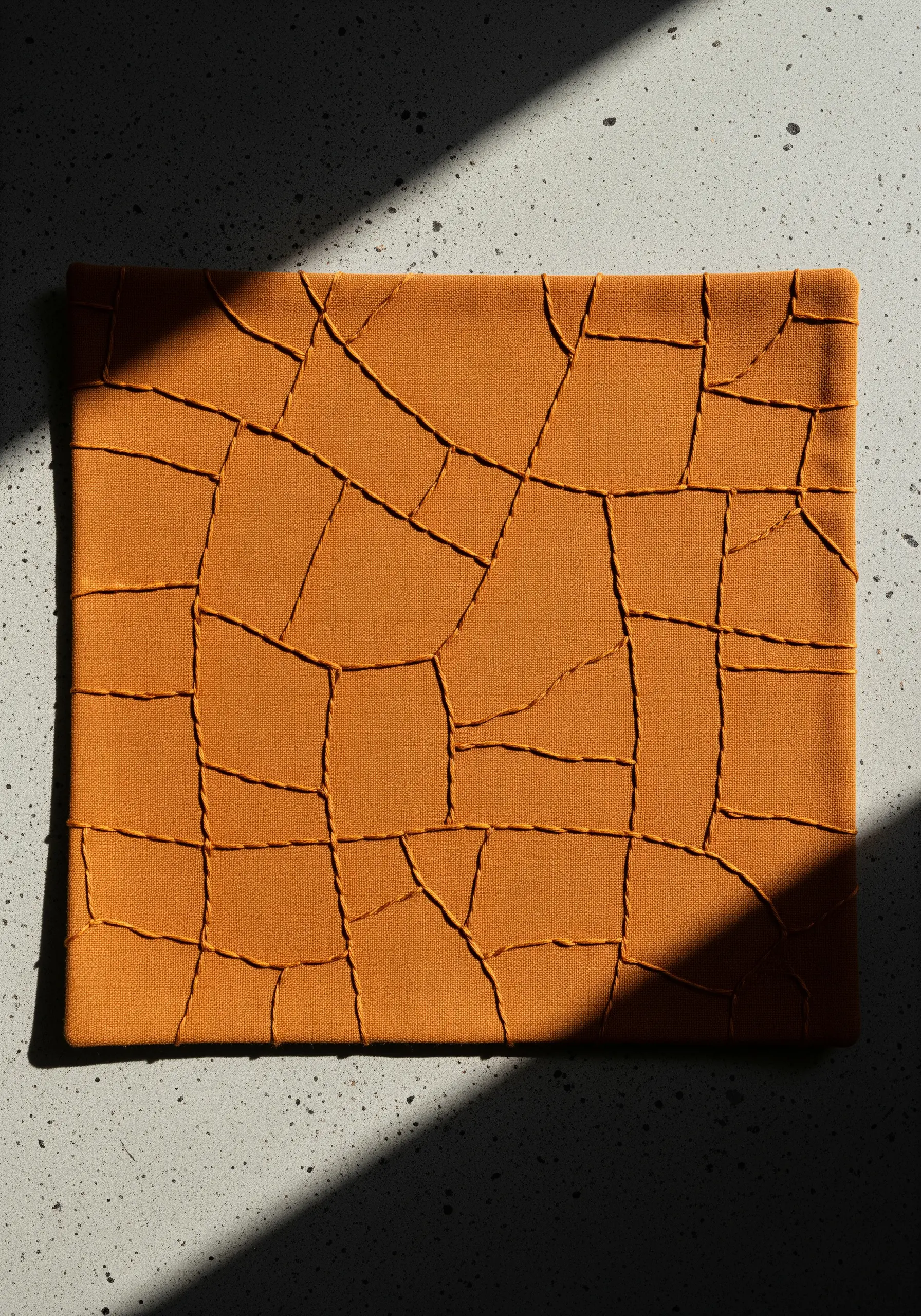 A square of orange fabric with raised, intersecting lines of thread that mimic cracked earth.