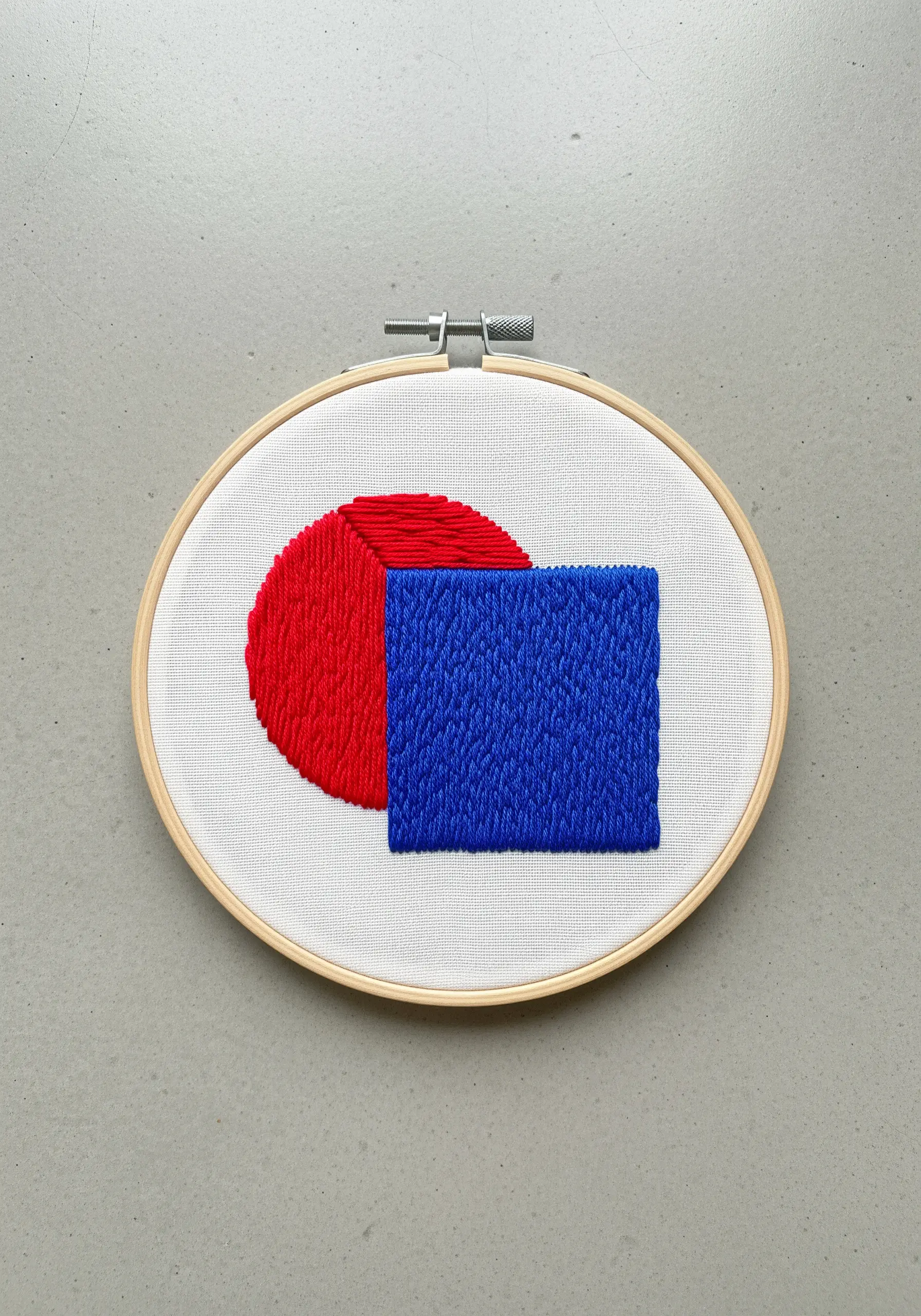 Abstract geometric embroidery with a red semi-circle and a blue rectangle in contrasting fill stitches.