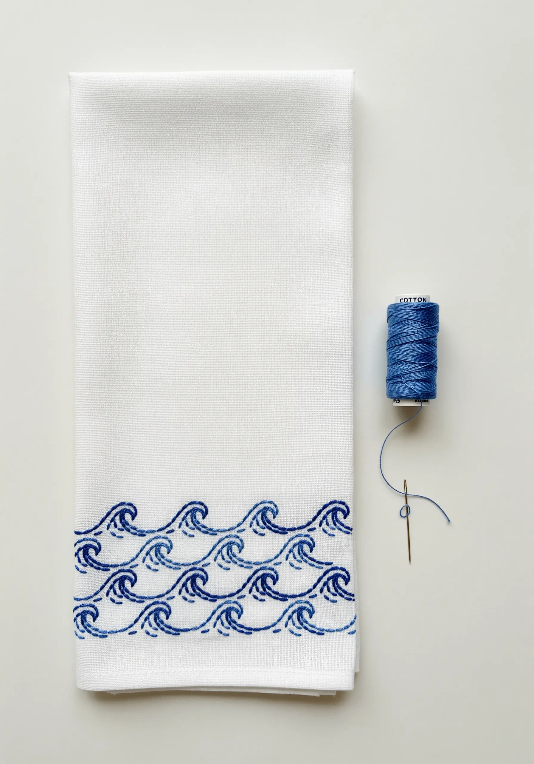 A border of stylized ocean waves embroidered in two shades of blue on a white towel.