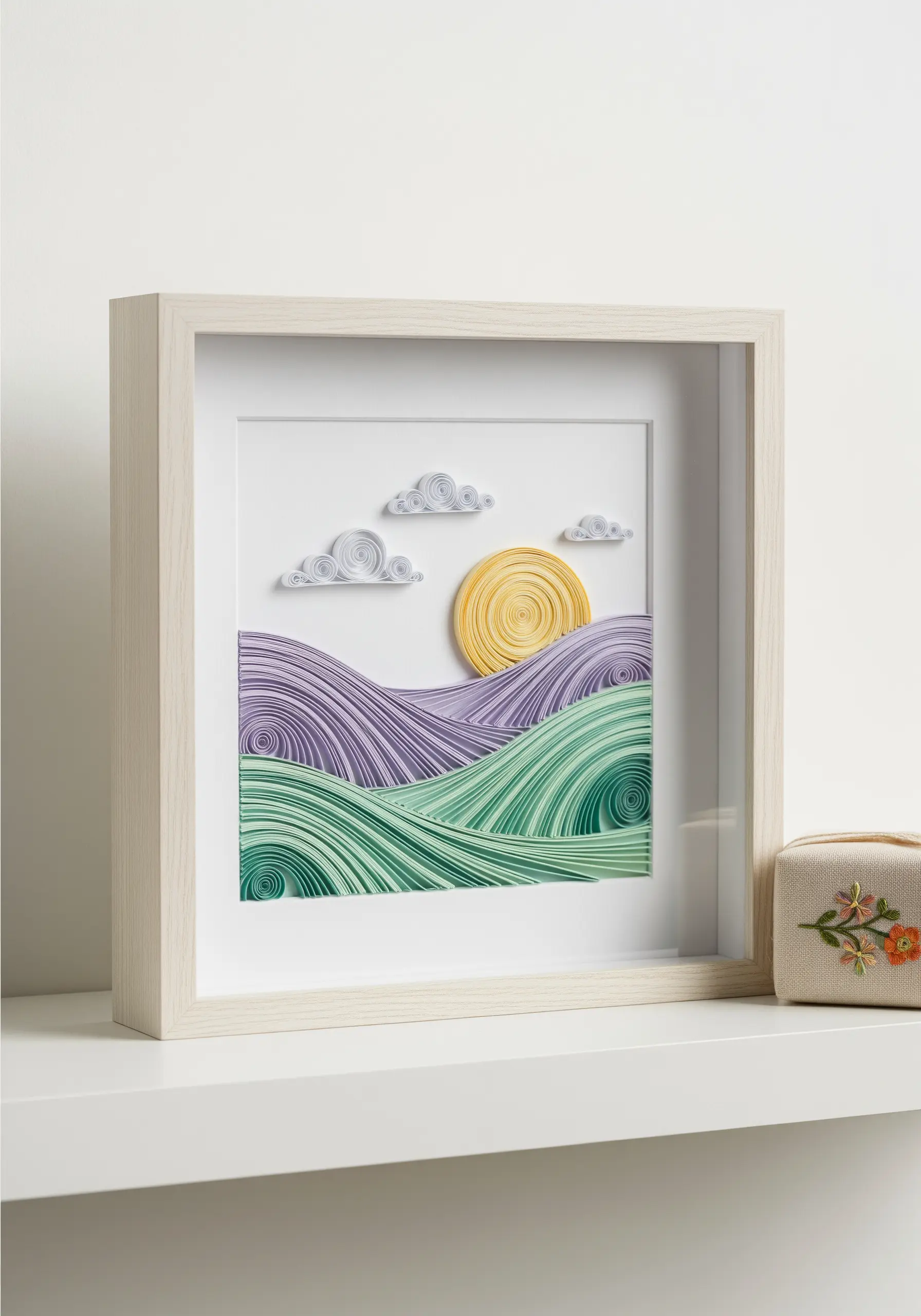 A framed paper quilling landscape depicting rolling hills, a sun, and clouds in a shadow box.