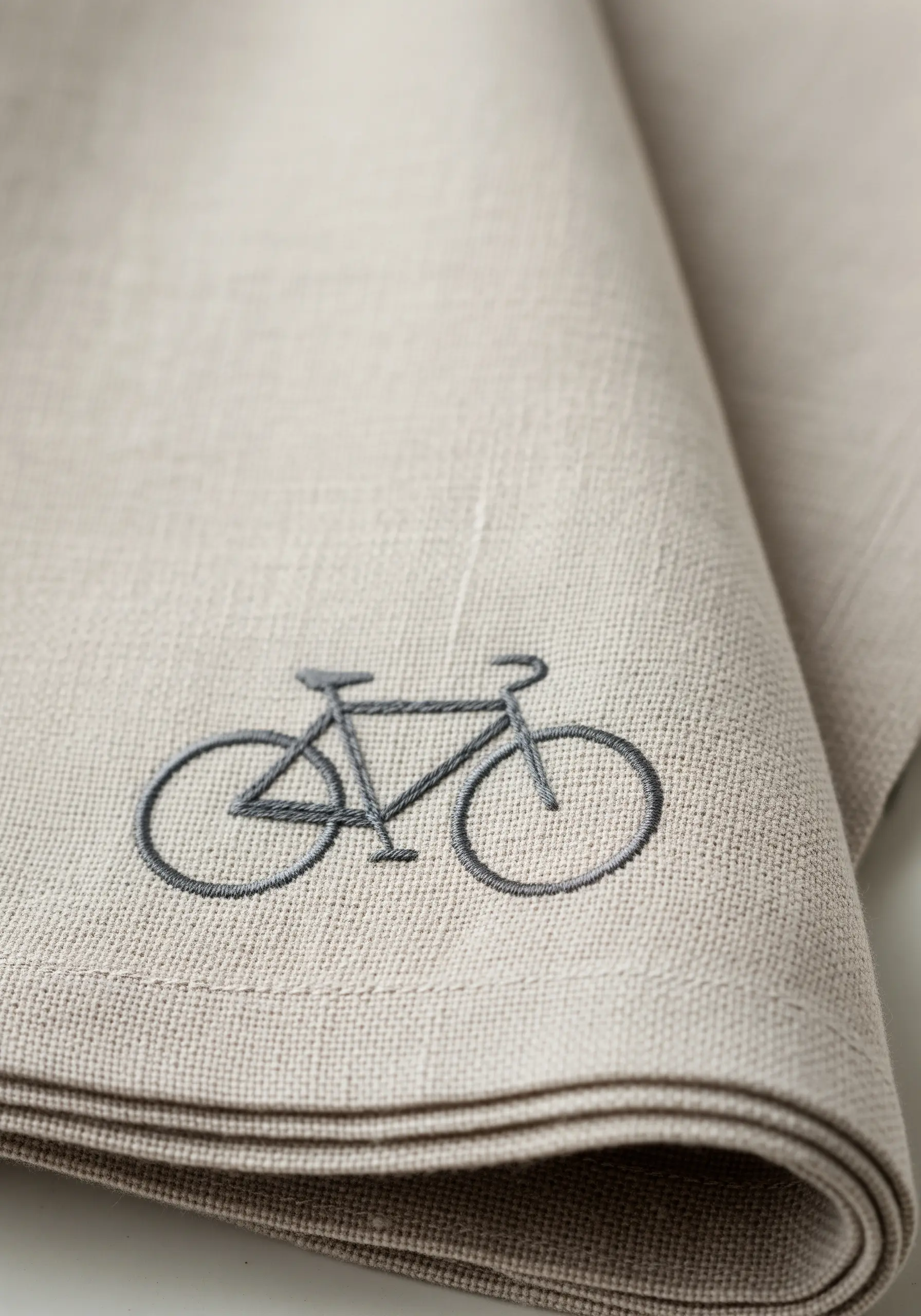A simple embroidered bicycle silhouette on a folded natural linen napkin.