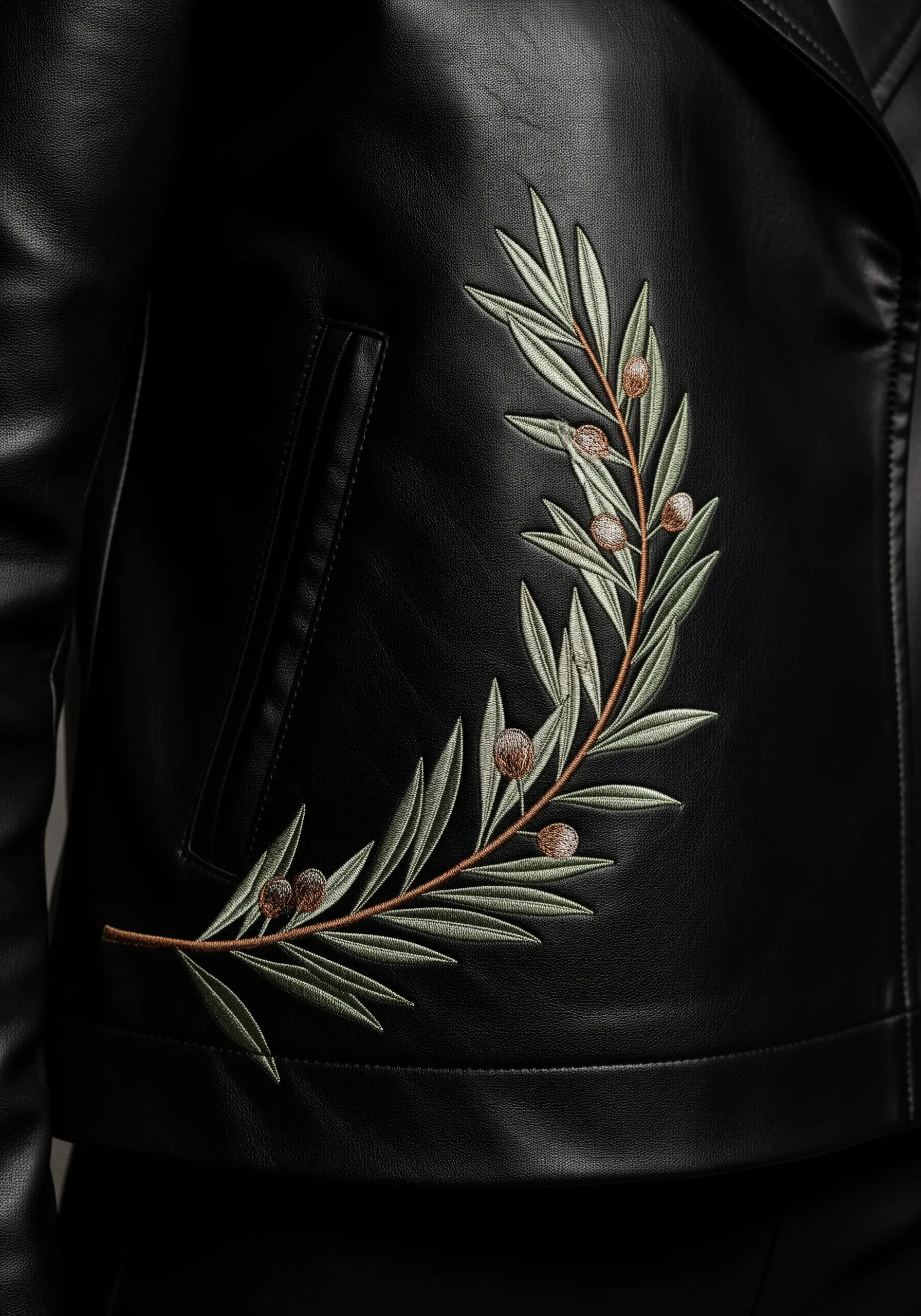 An embroidered olive branch with sage green leaves on a black leather jacket.