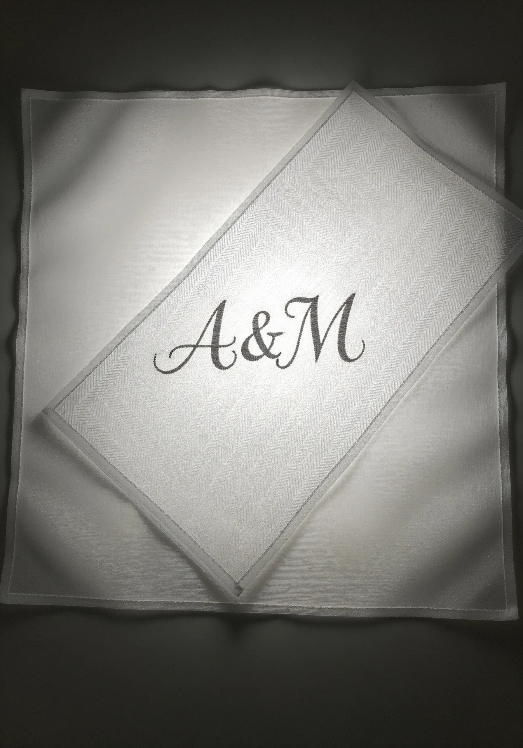 A simple 'A&M' monogram in charcoal thread on a white herringbone placemat.