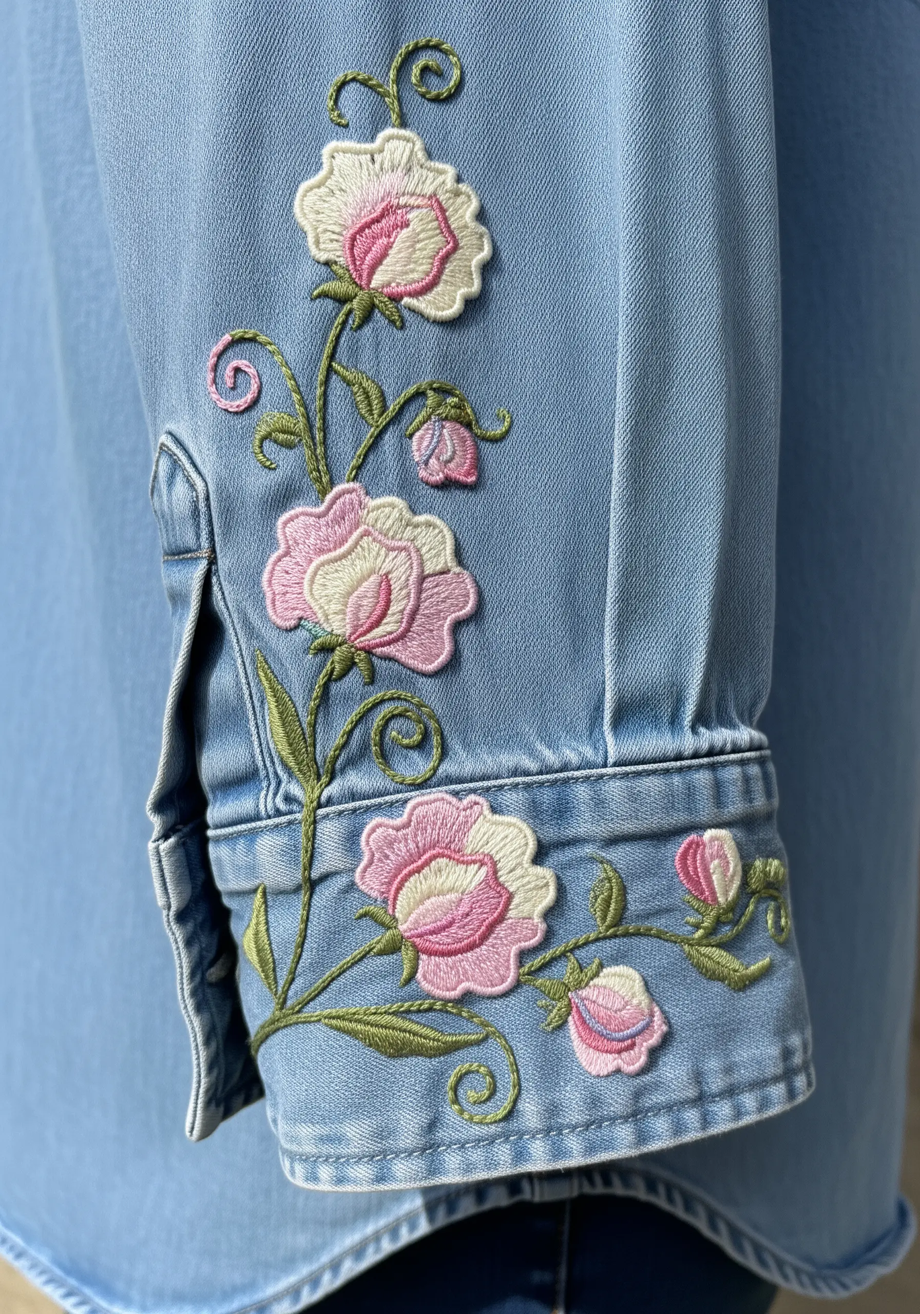 Pink and white raised satin stitch flowers climbing up the cuff of a chambray shirt.