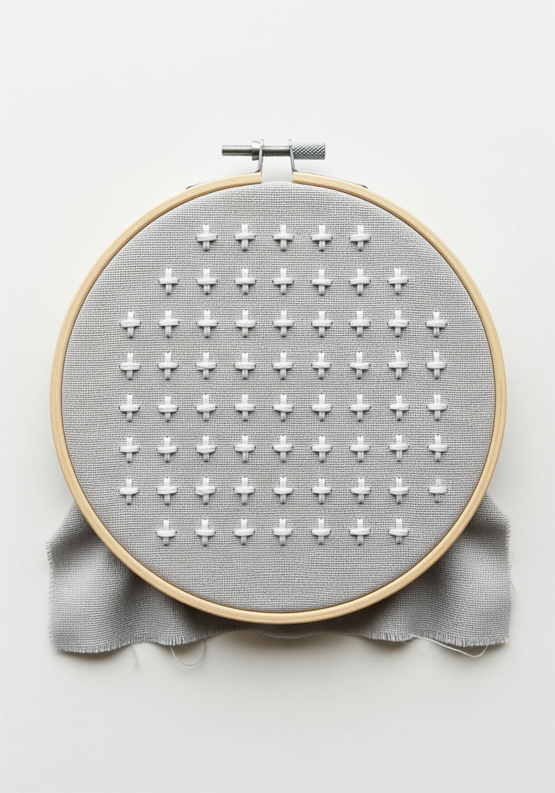 A grid of raised white cross stitches, creating a textured pattern on grey fabric.