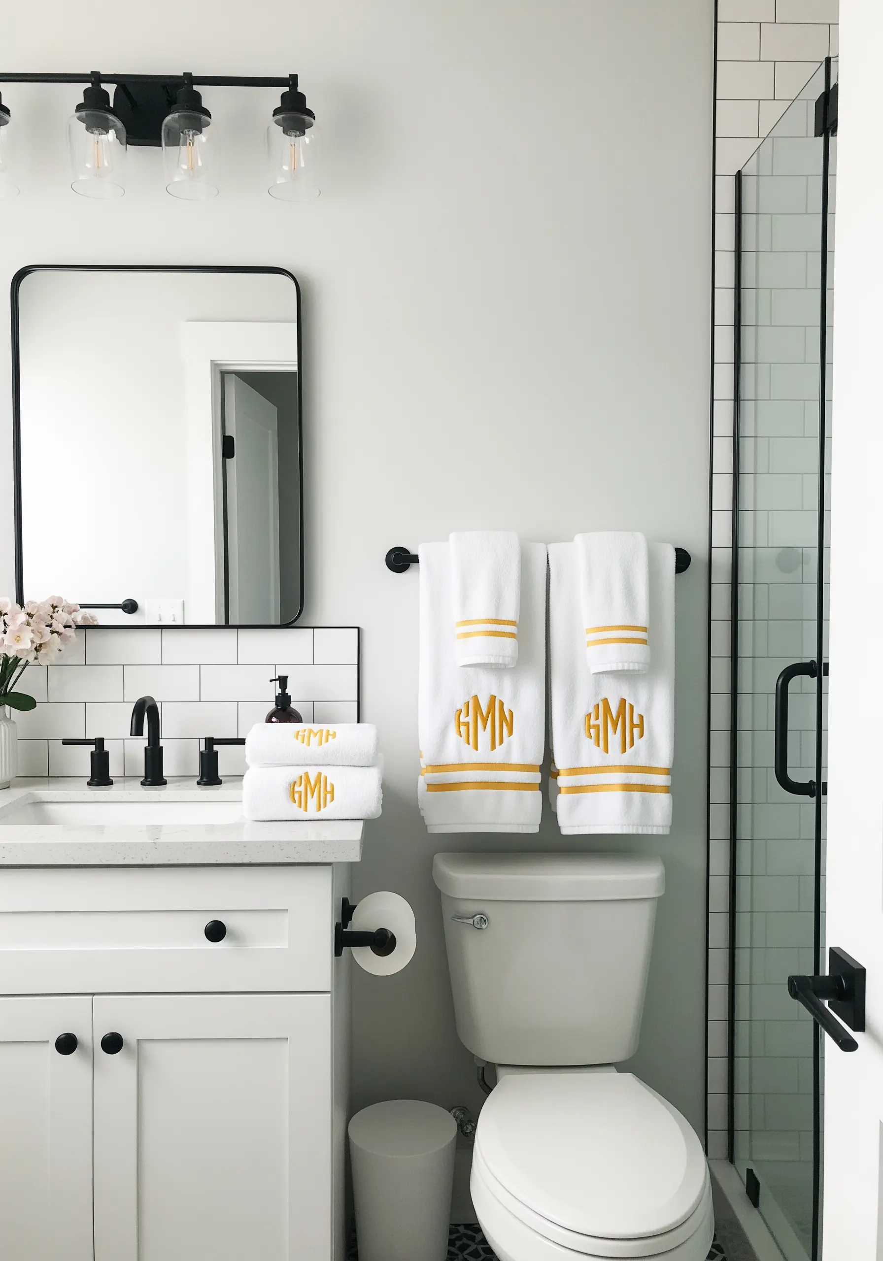 White bathroom towels with a bold, modern gold embroidered monogram hanging over a toilet.