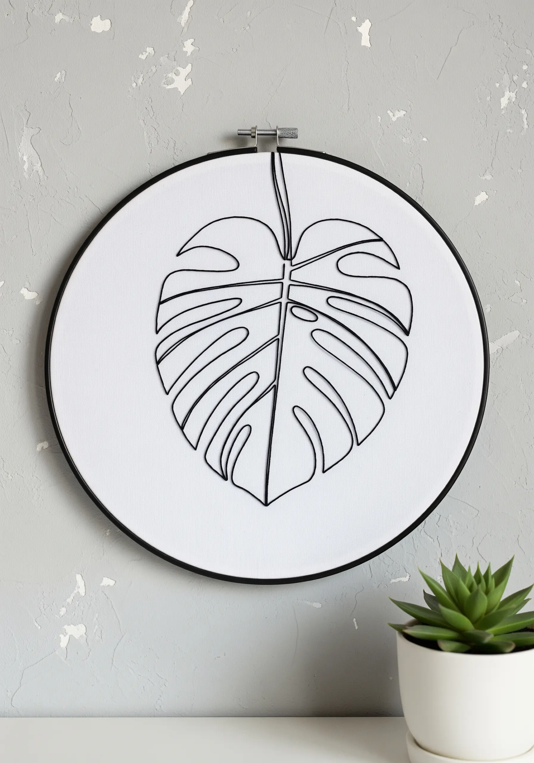 Minimalist black-thread outline of a monstera leaf on crisp white fabric in a black hoop.