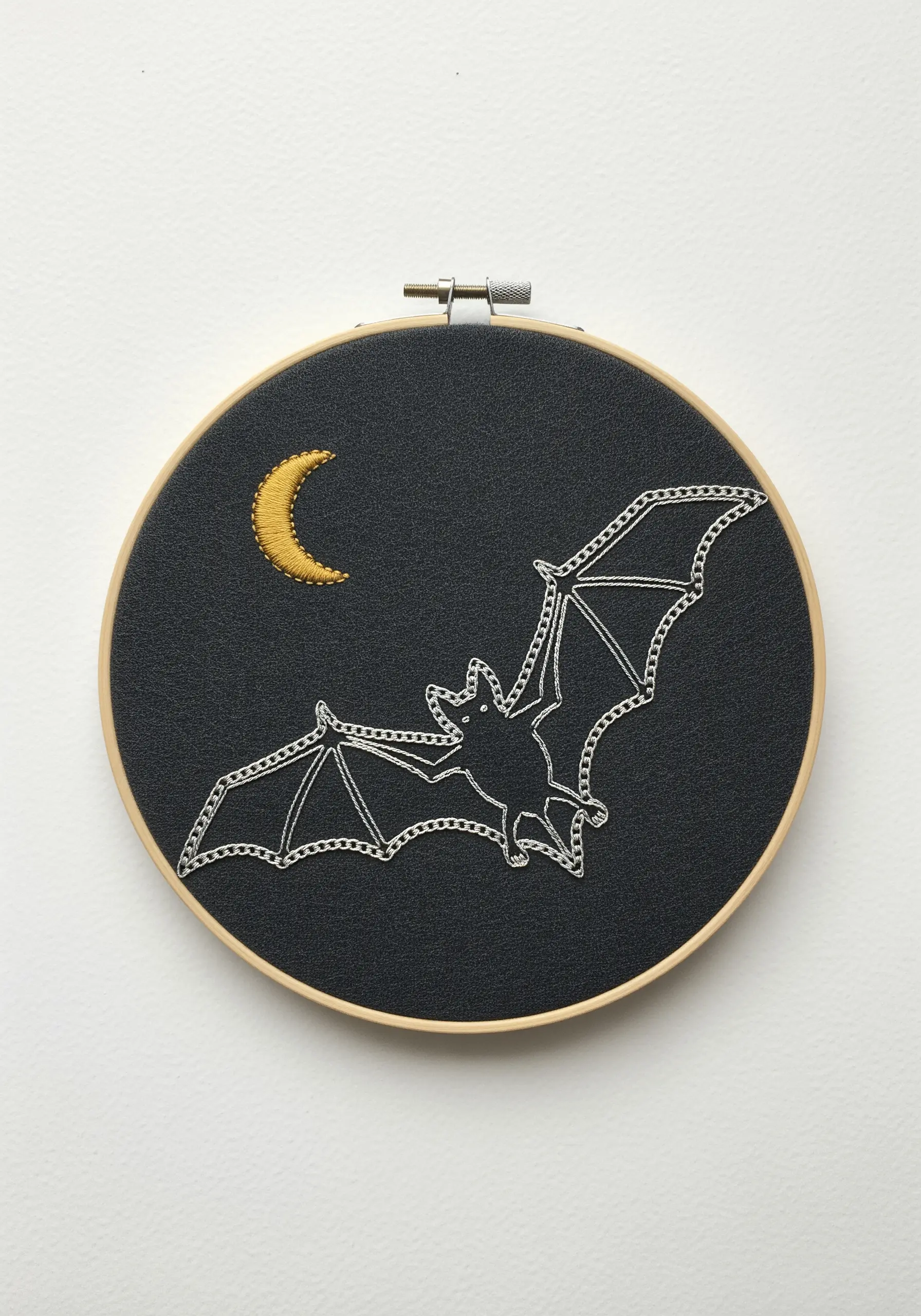 Minimalist line art embroidery of a bat and crescent moon on dark grey fabric.