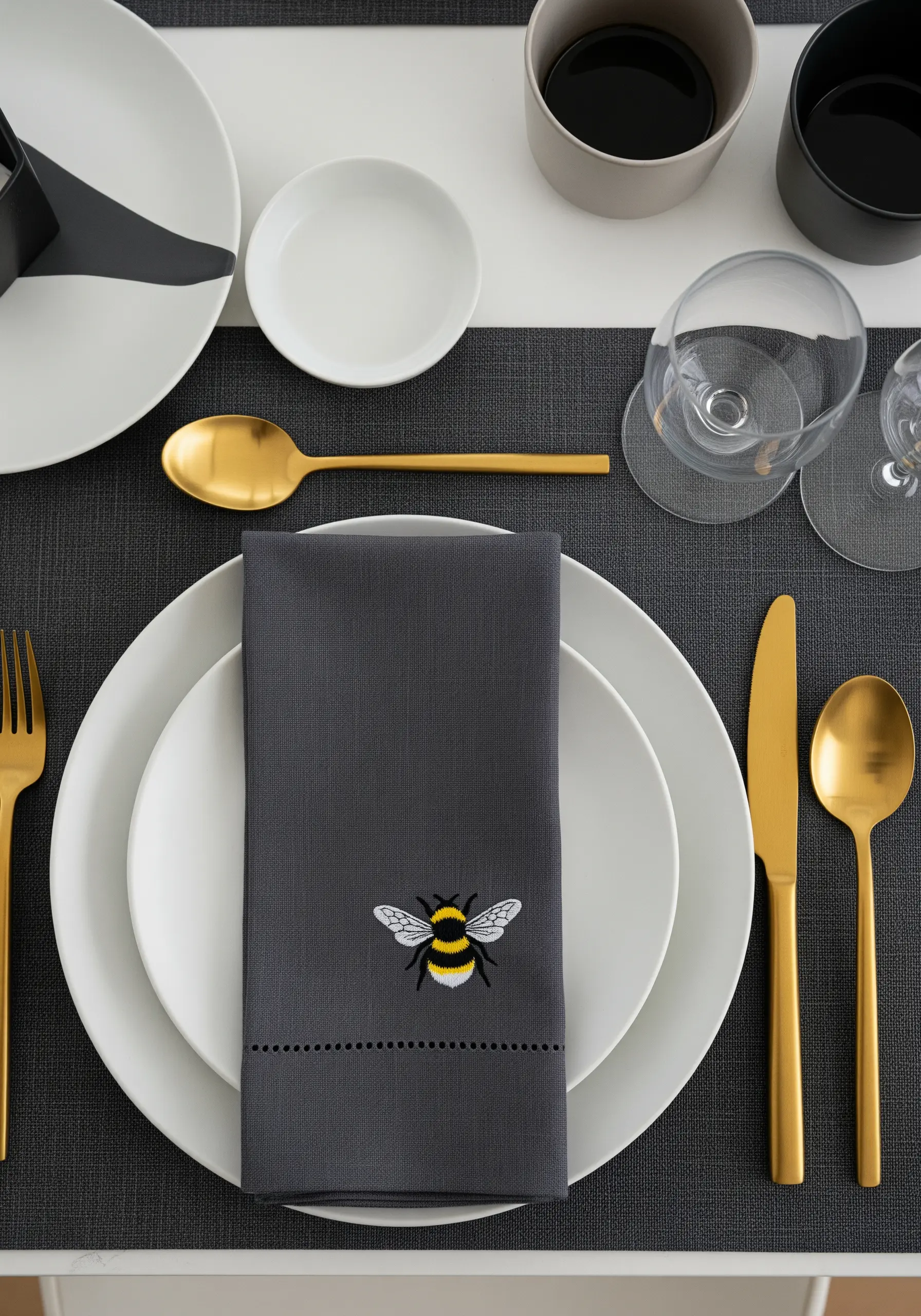 A finely detailed embroidered bee with translucent wings on a dark grey linen napkin.