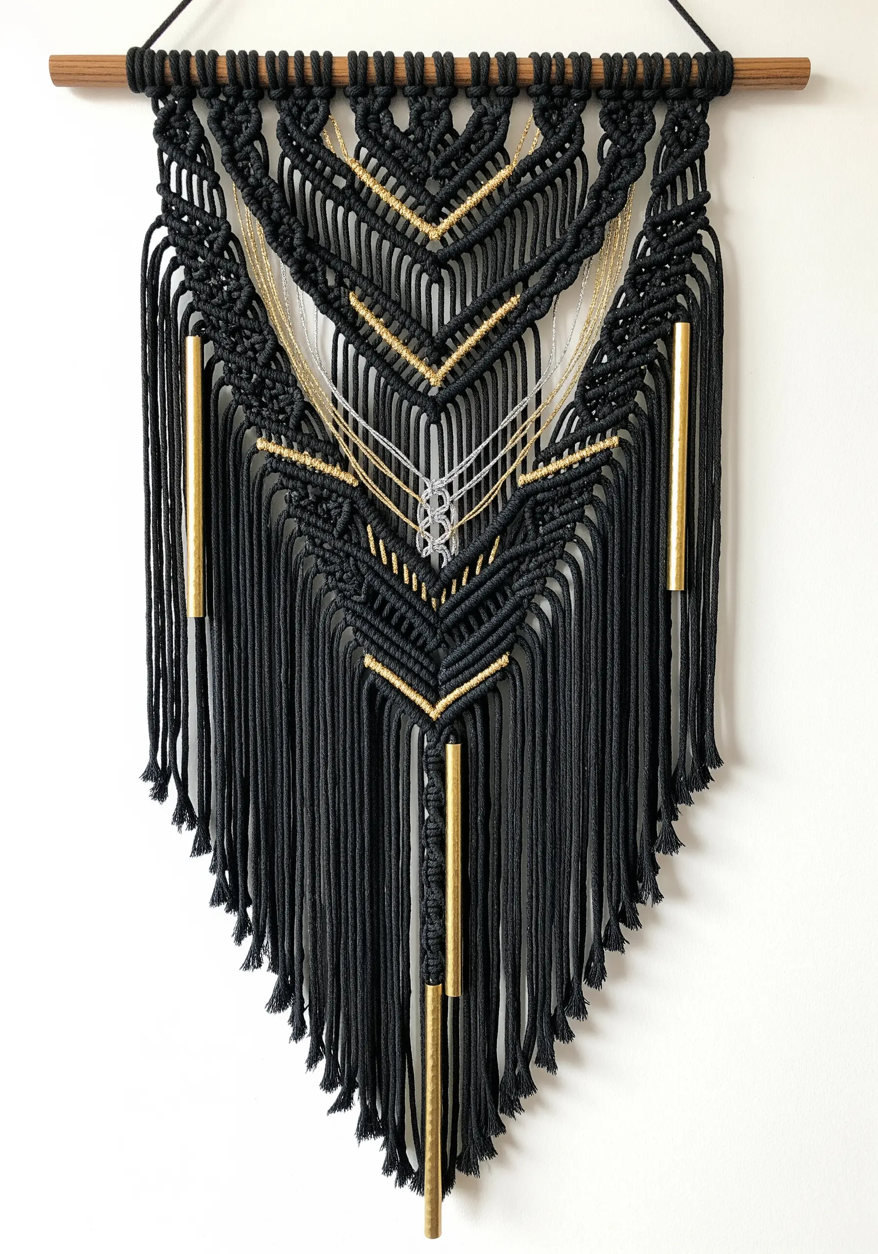 An intricate black macrame wall hanging with integrated gold and silver threads and polished brass tubes.