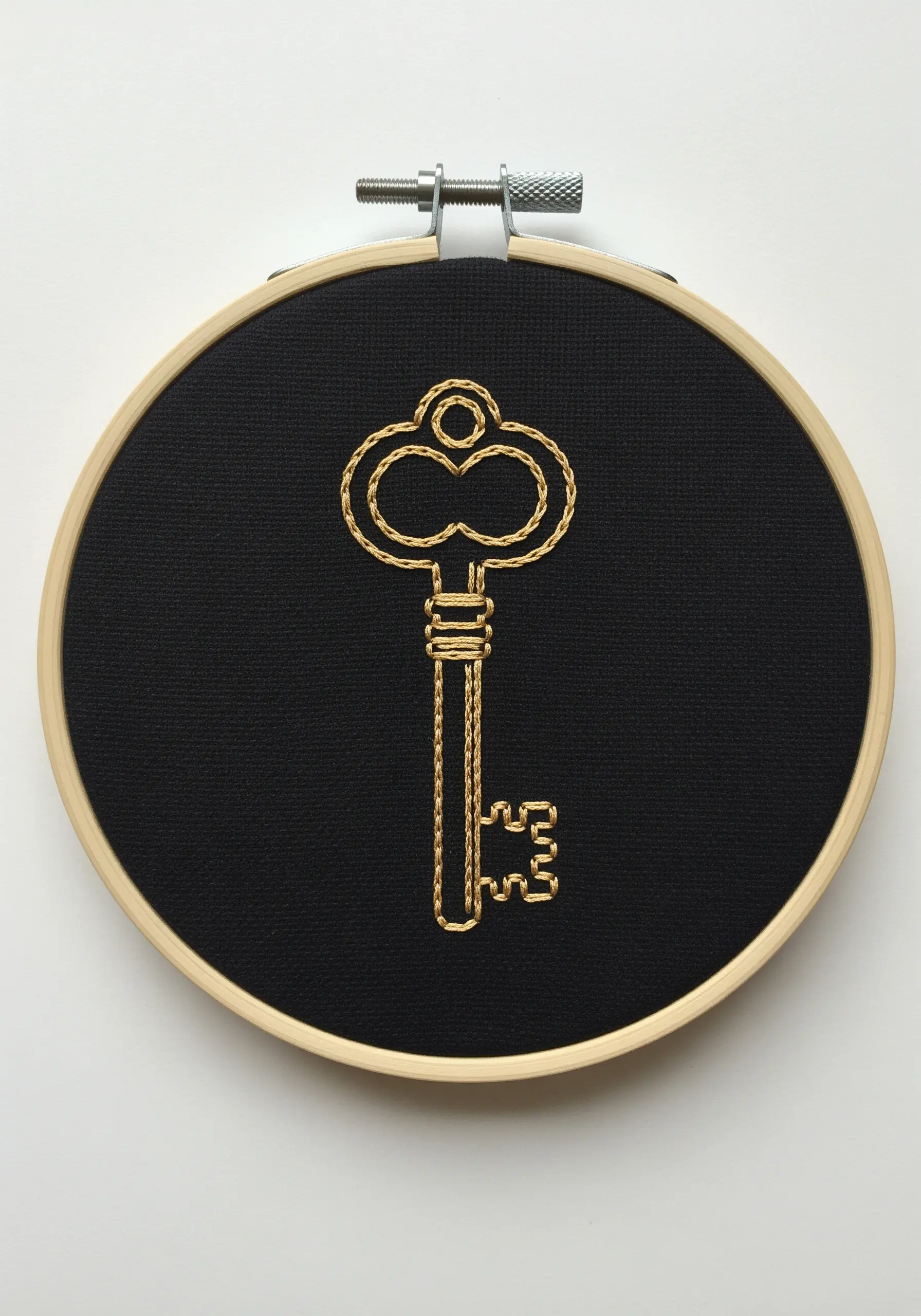 An ornate key outlined in gold metallic thread on a solid black fabric background.