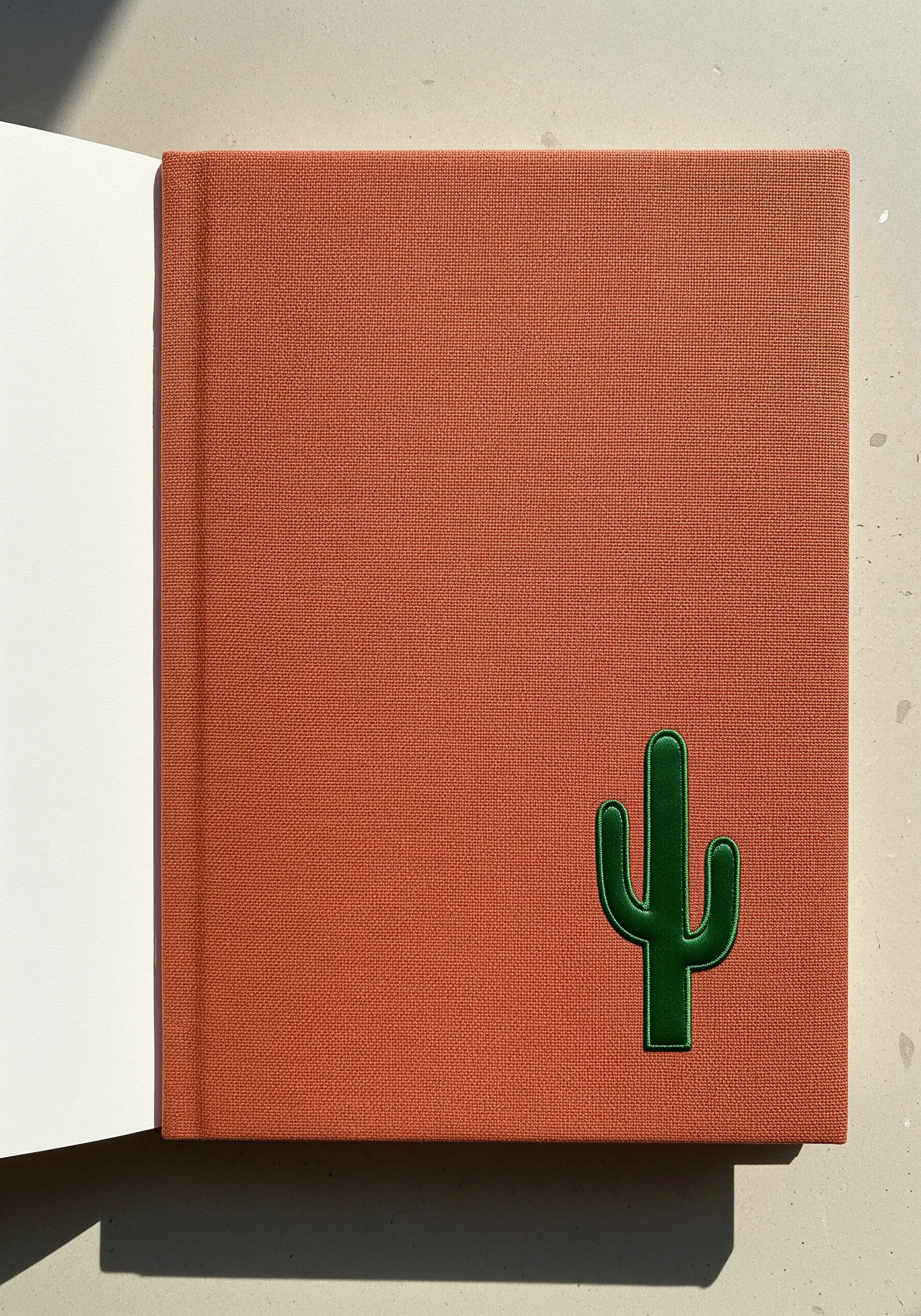 A padded satin stitch cactus in dark green on a terracotta-colored notebook.