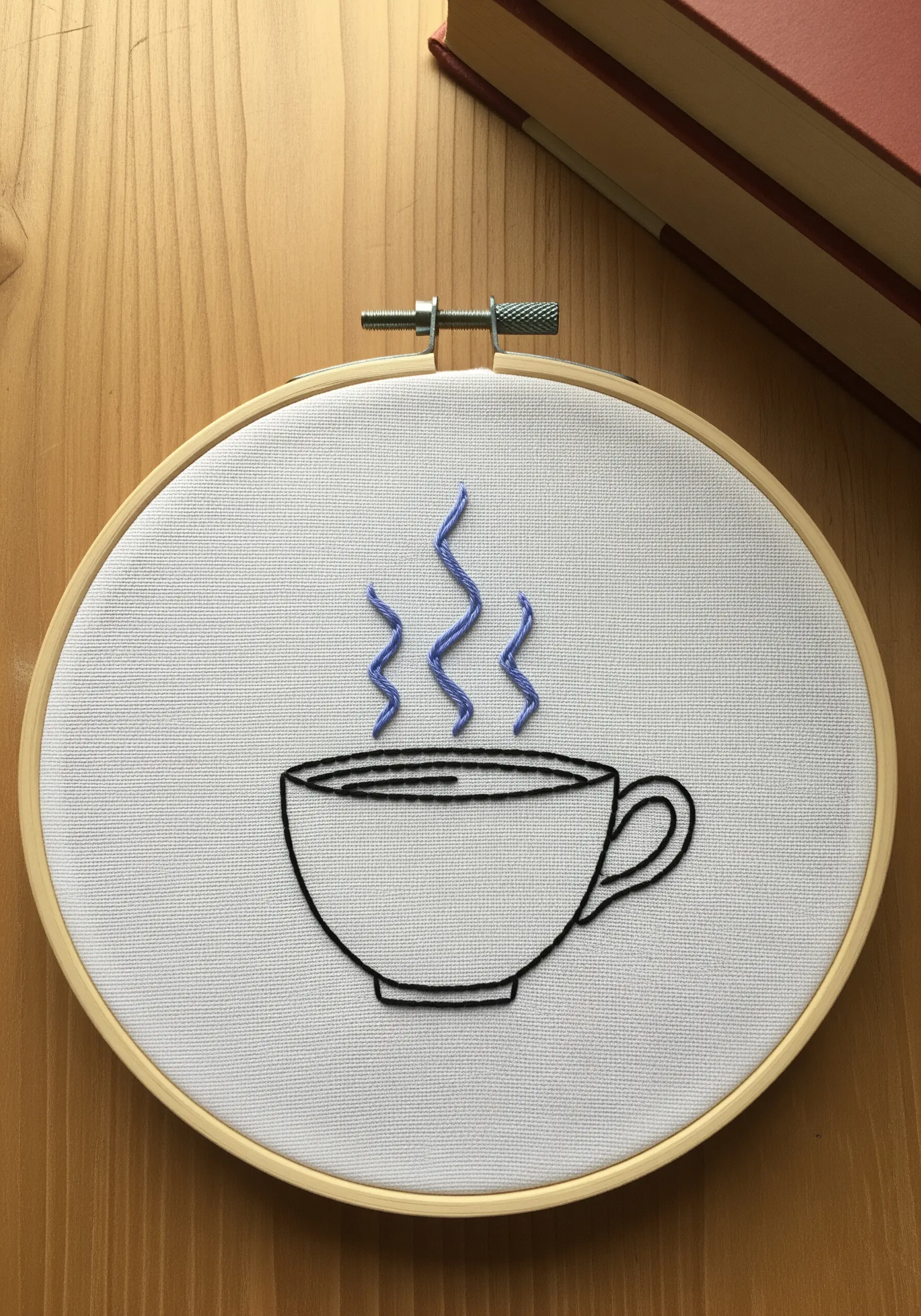 Minimalist line art embroidery of a coffee cup with blue steam.