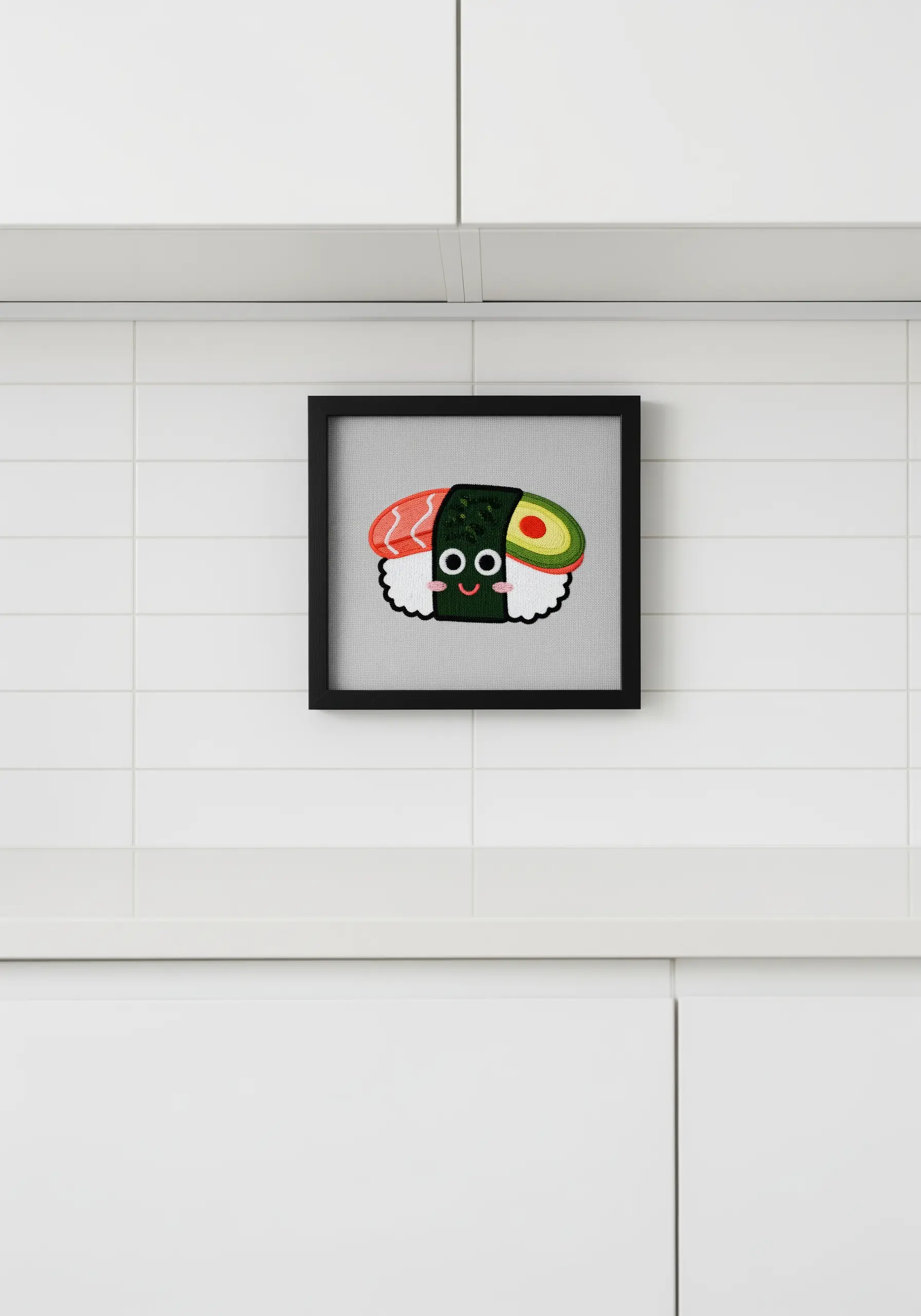 A cute, smiling sushi character embroidered and framed on a white tiled kitchen wall.