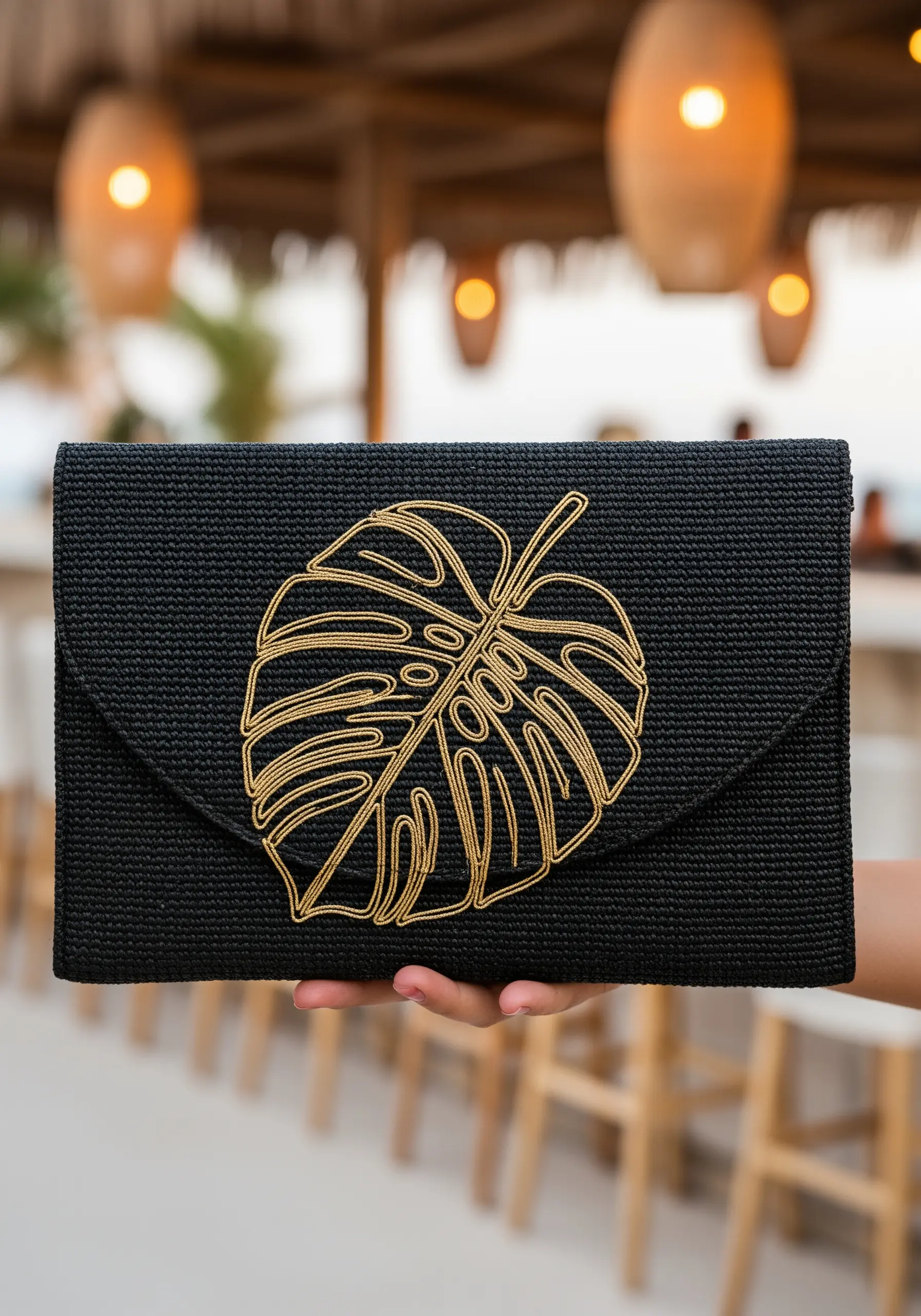 A graphic gold metallic thread monstera leaf embroidered on a black straw clutch.