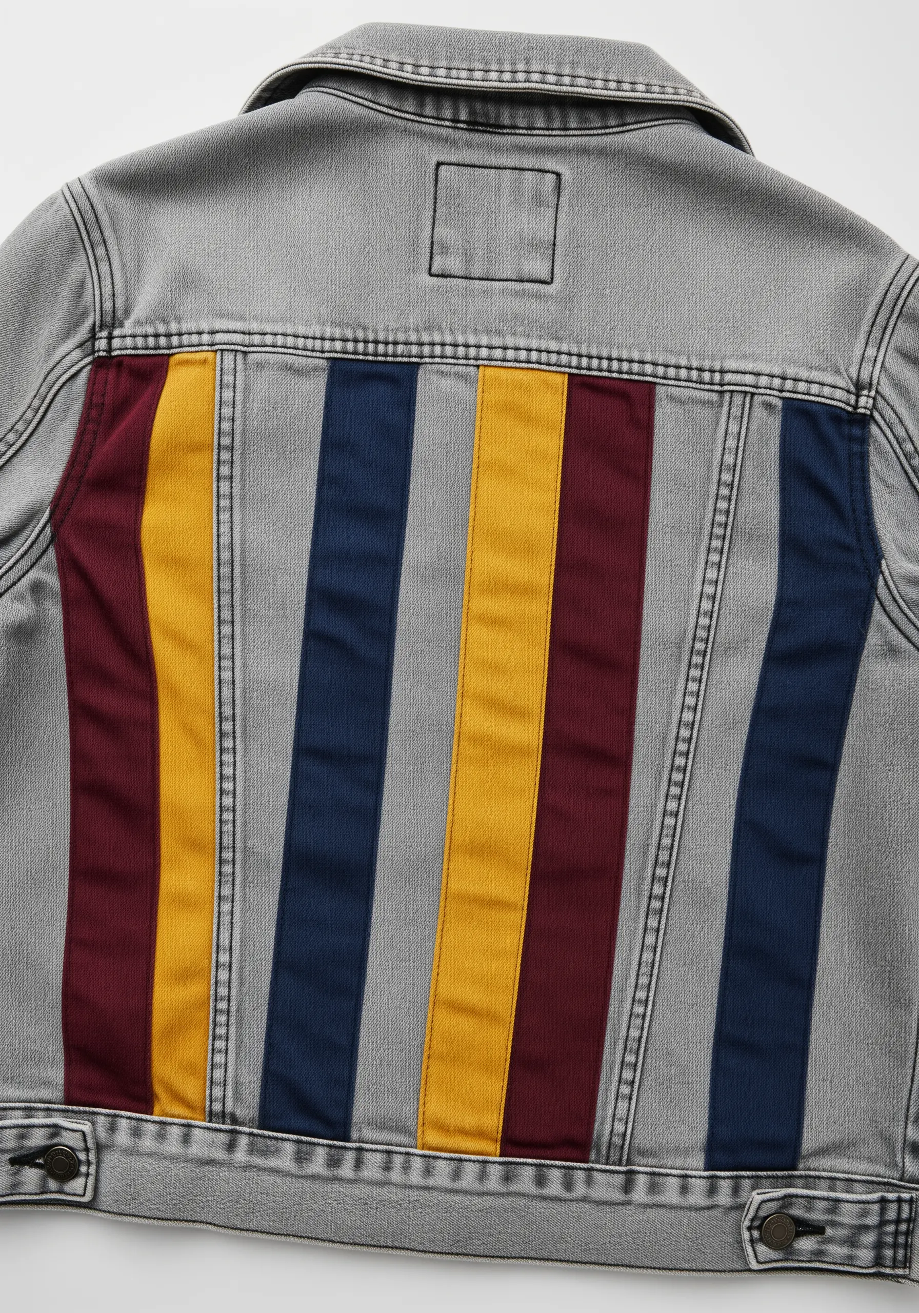 Vertical panels of color-blocked fabric in red, yellow, and blue on a grey denim jacket.